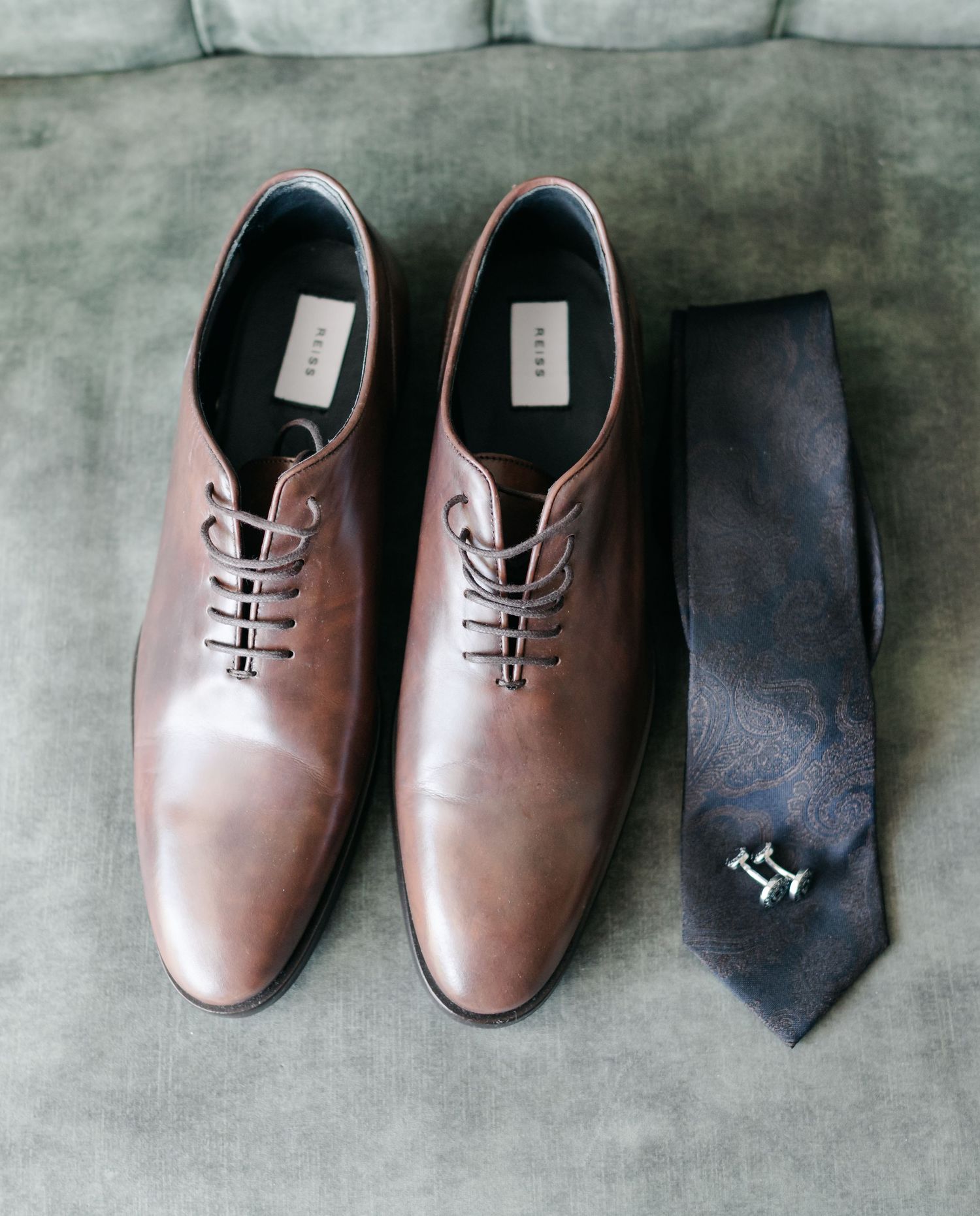 Brown leather oxford dress shoes and a navy blue necktie arranged in a row on a gray textured surface.