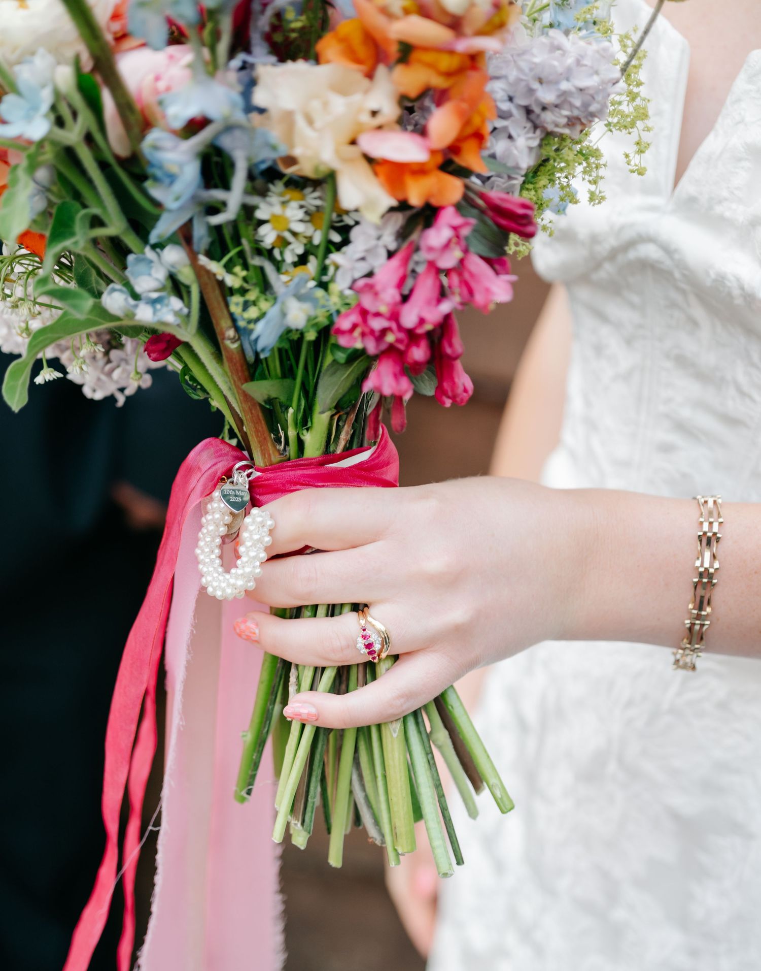 Close-up of hands holding a vibrant spring wedding bouquet with pink and orange flowers.