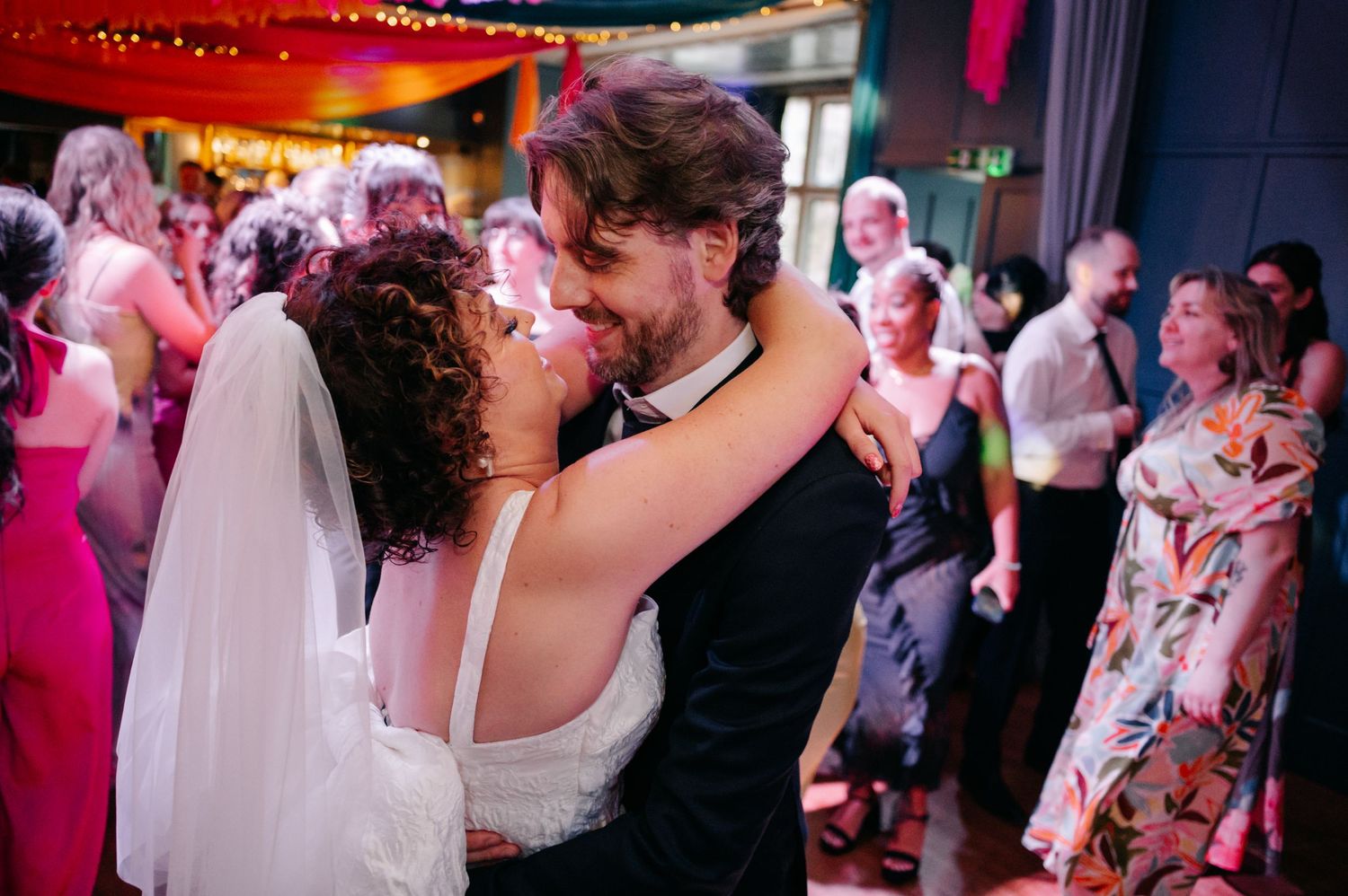 Wedding reception dance floor filled with celebration under red ambient lighting.
