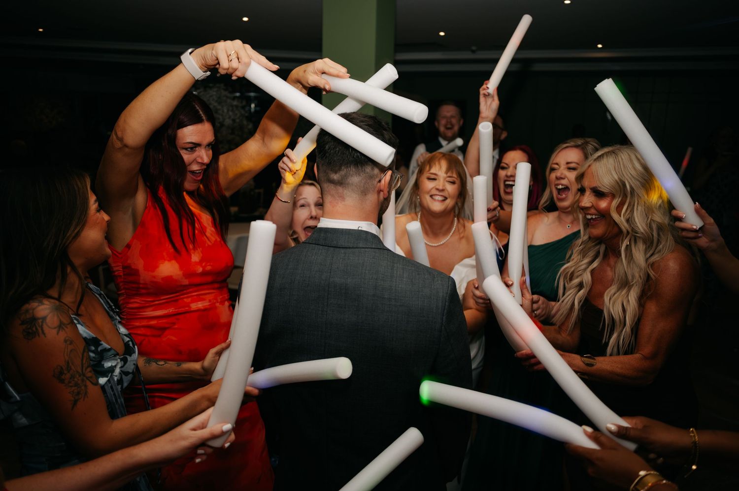 Wedding guests dancing and celebrating with glow sticks on a dark dance floor.