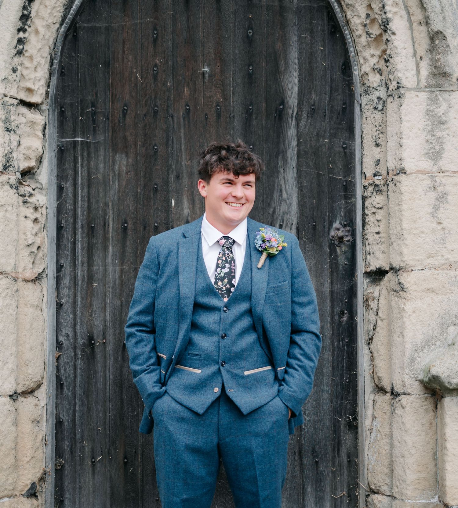 Wedding couple poses against rustic wooden church doors in navy blue suit and white dress.