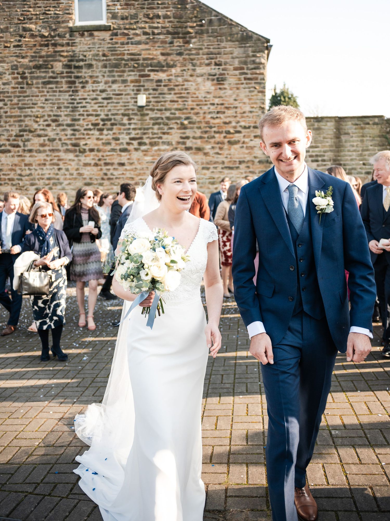 Joyful wedding couple walking together outside a rustic brick building.