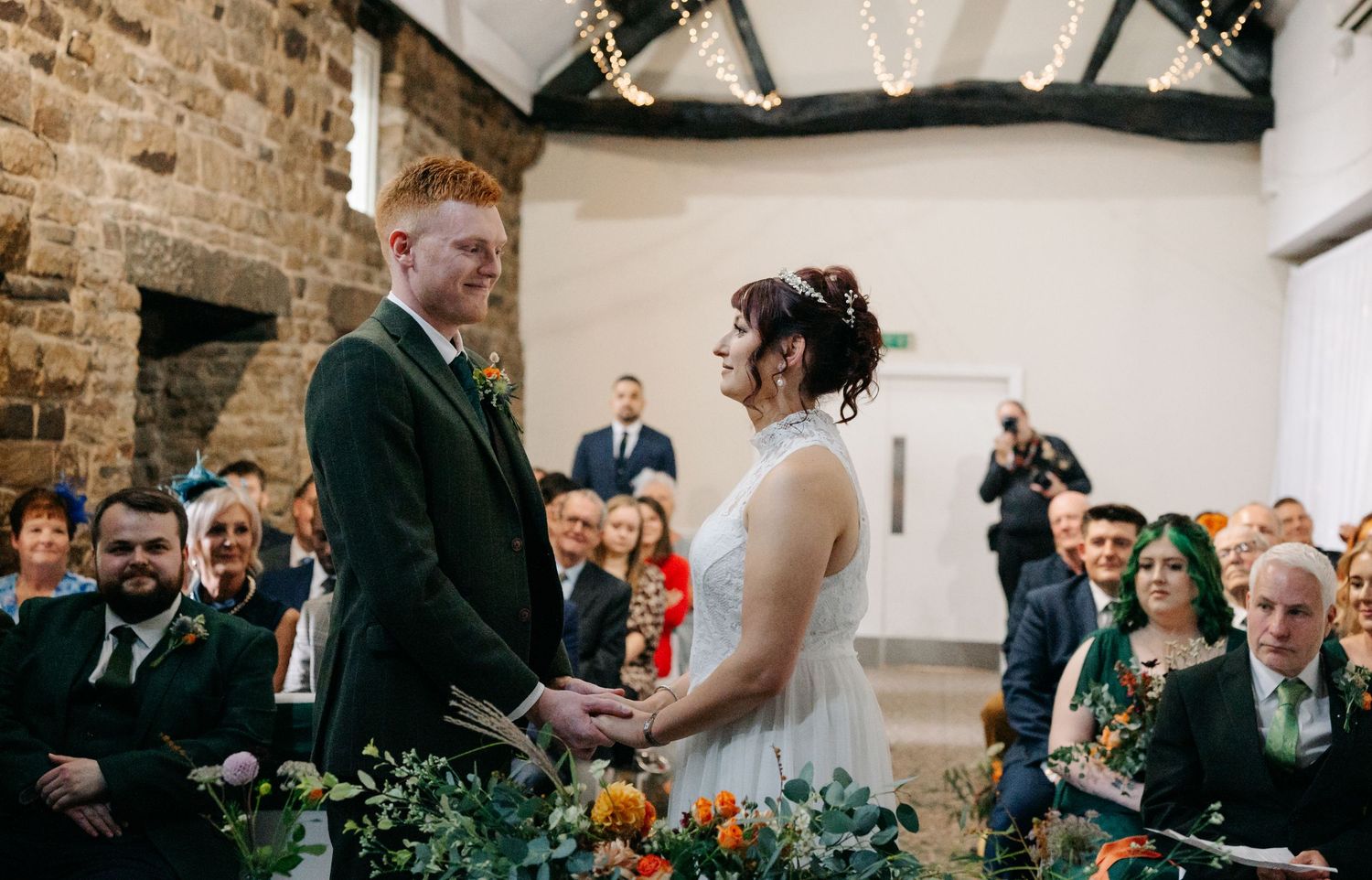 Wedding ceremony in rustic stone venue with floral decorations and guests seated.