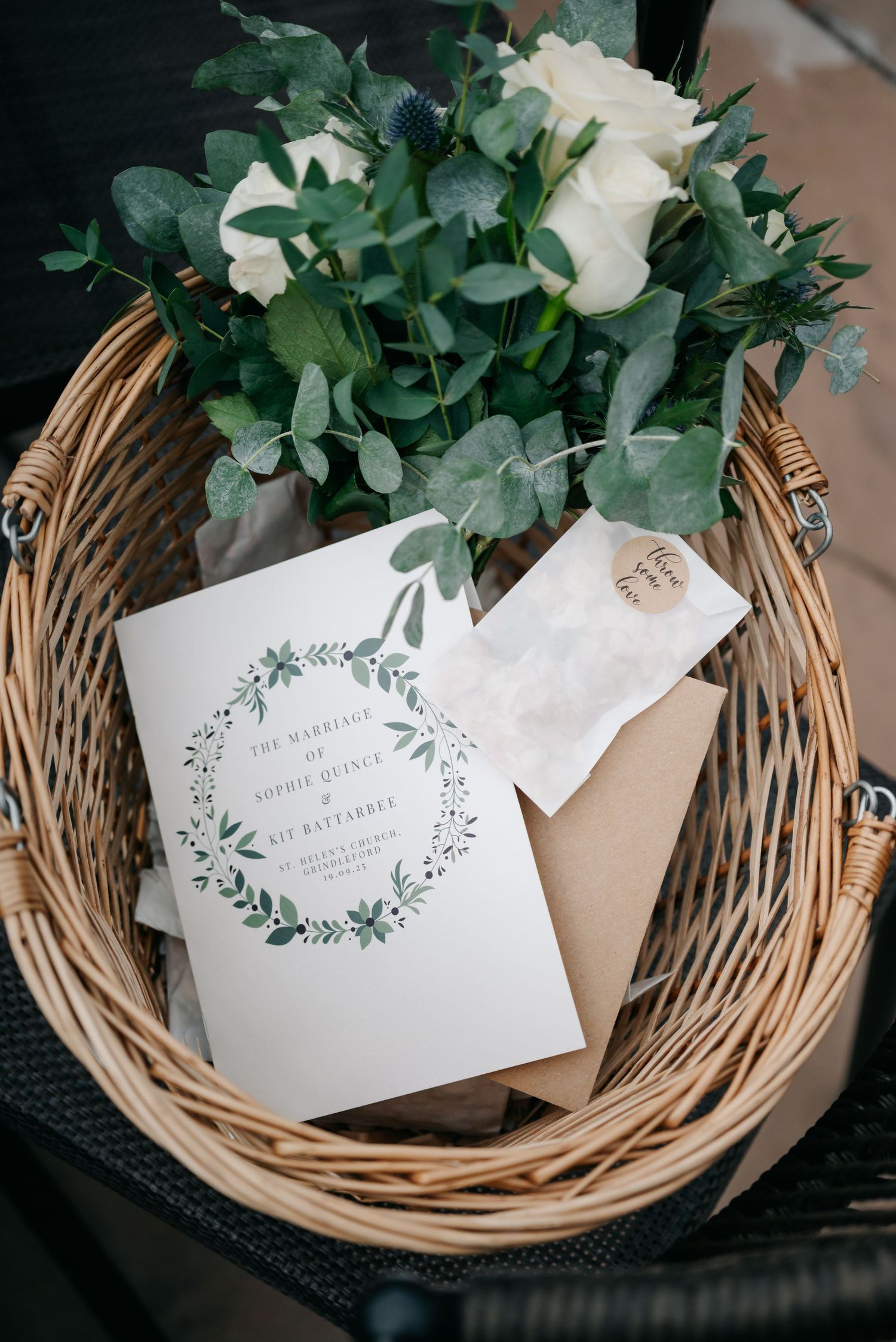 Wedding invitations and greenery arranged in wicker basket.