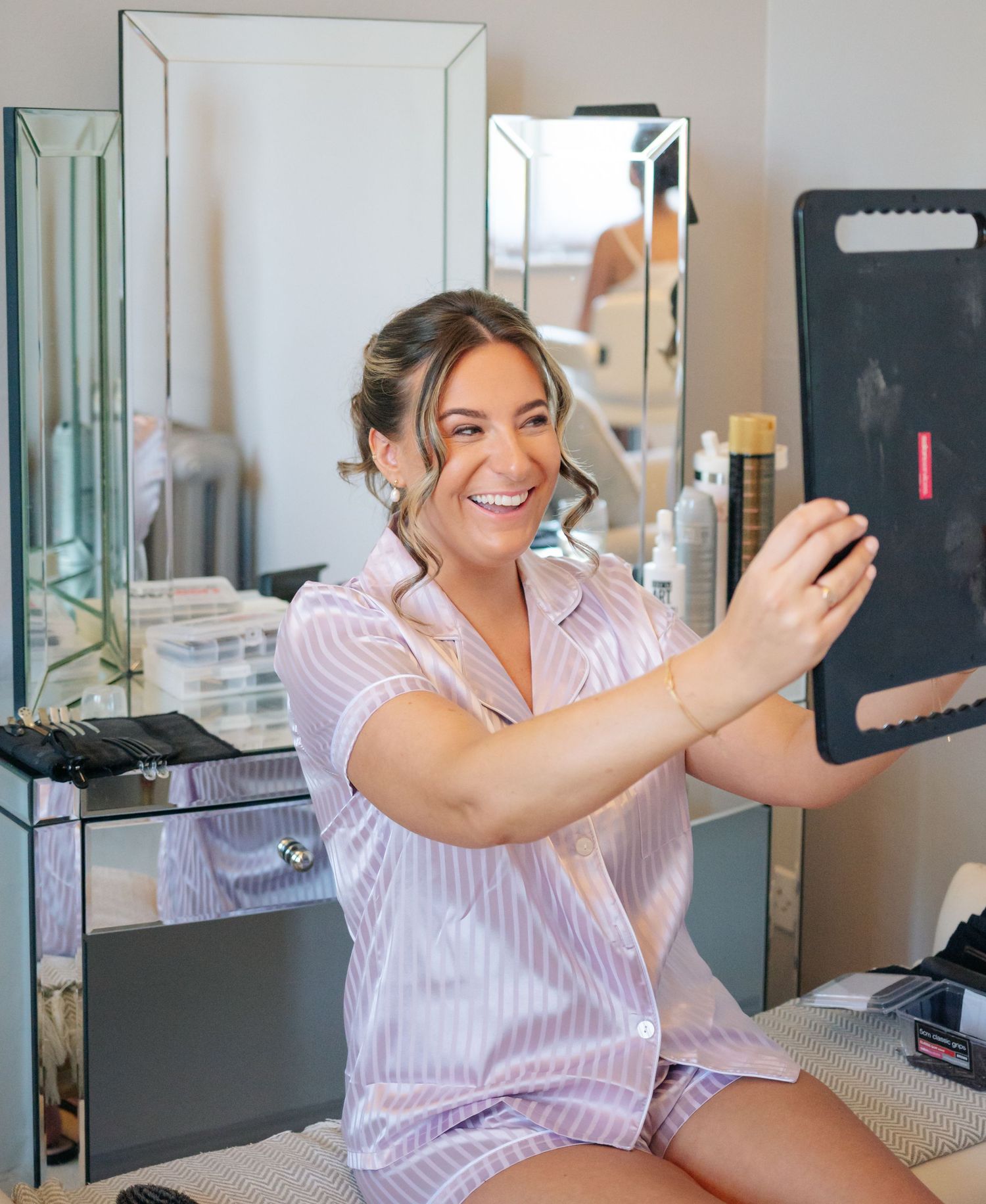 Woman in pink striped pajamas taking selfies and smiling while sitting on bed in bedroom.