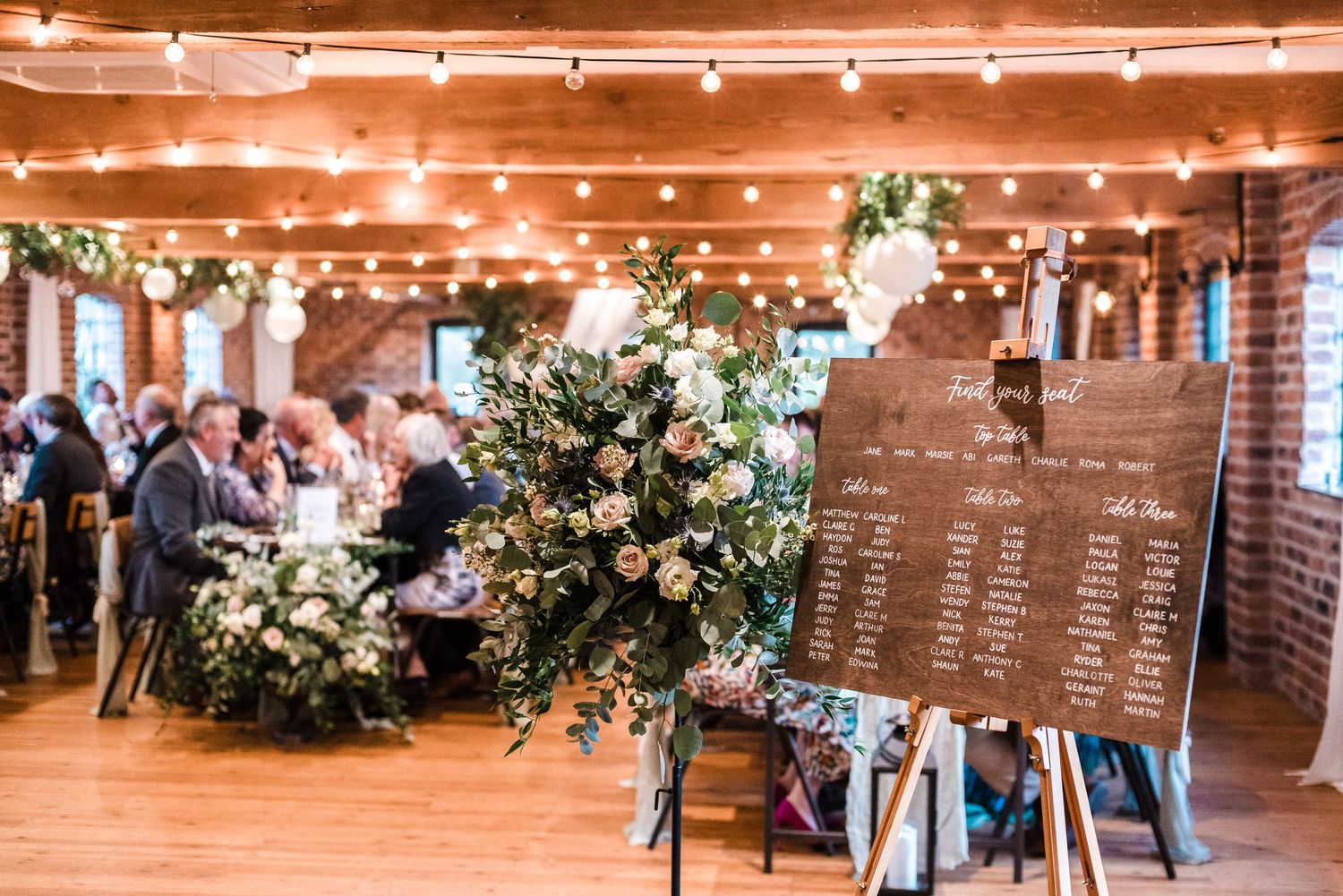 Reception venue decorated with string lights, floral arrangements and seating chart display.