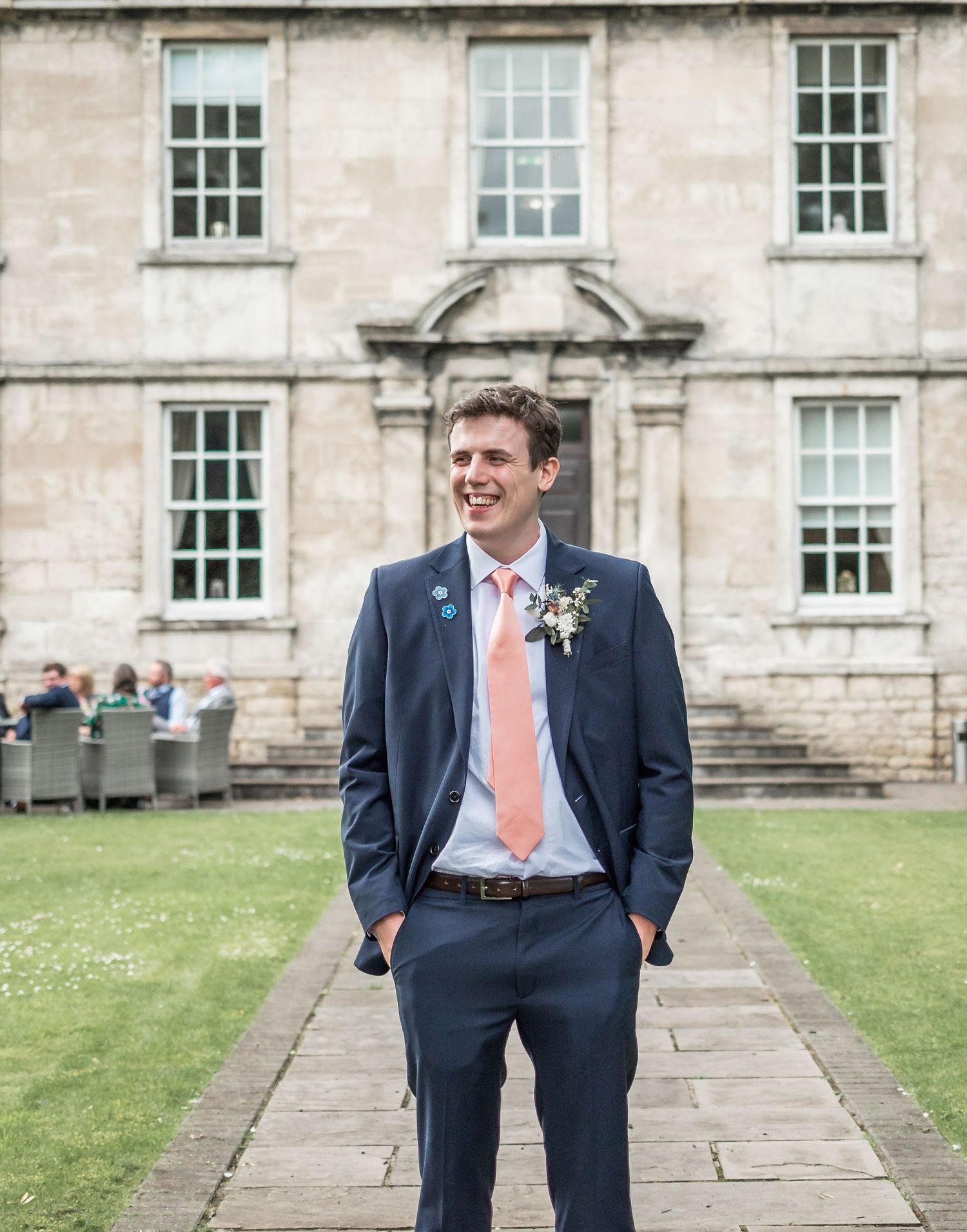 Elegant stone building facade with a groom in navy suit standing on stone pathway.