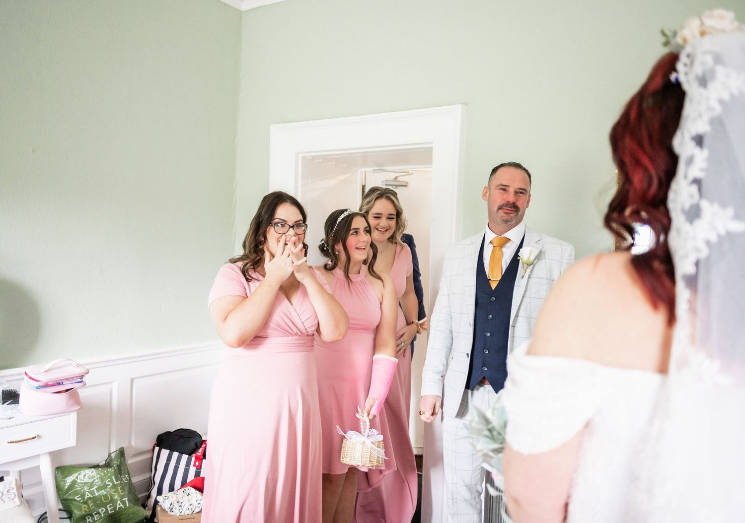 Wedding party members in pink dresses react emotionally to seeing the bride.