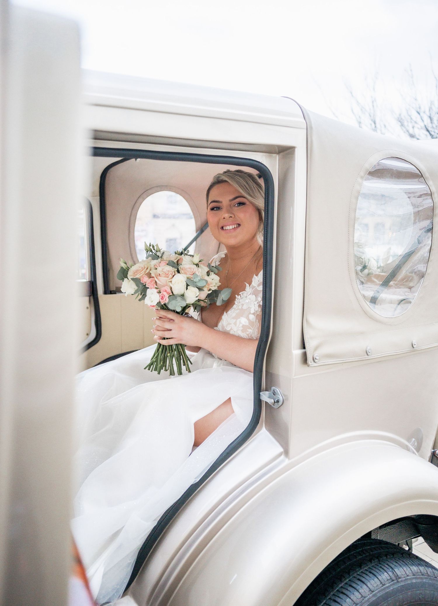 Classic white vintage car with bridal bouquet visible through open door.