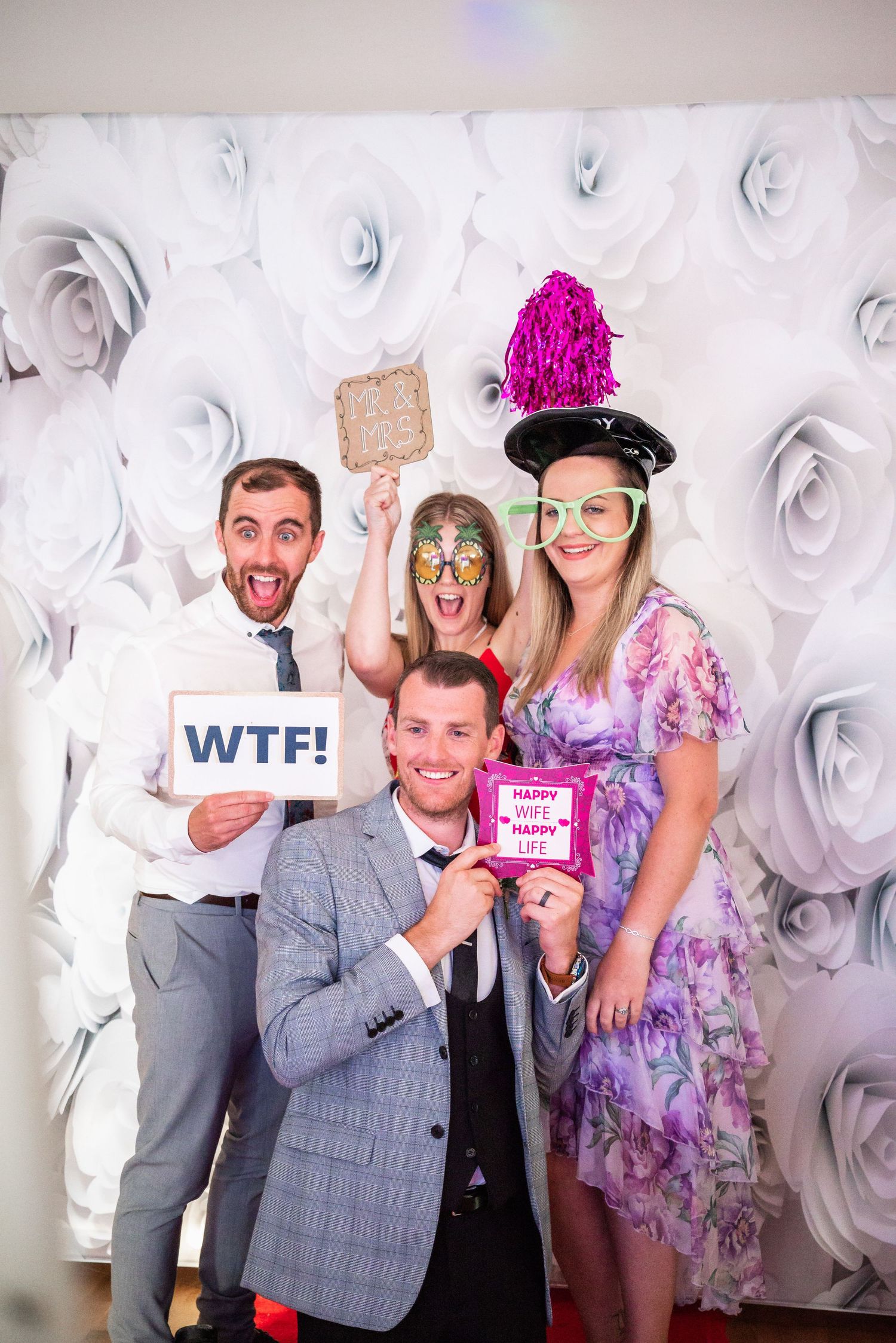 Group photo with props against a white floral backdrop at a wedding reception.