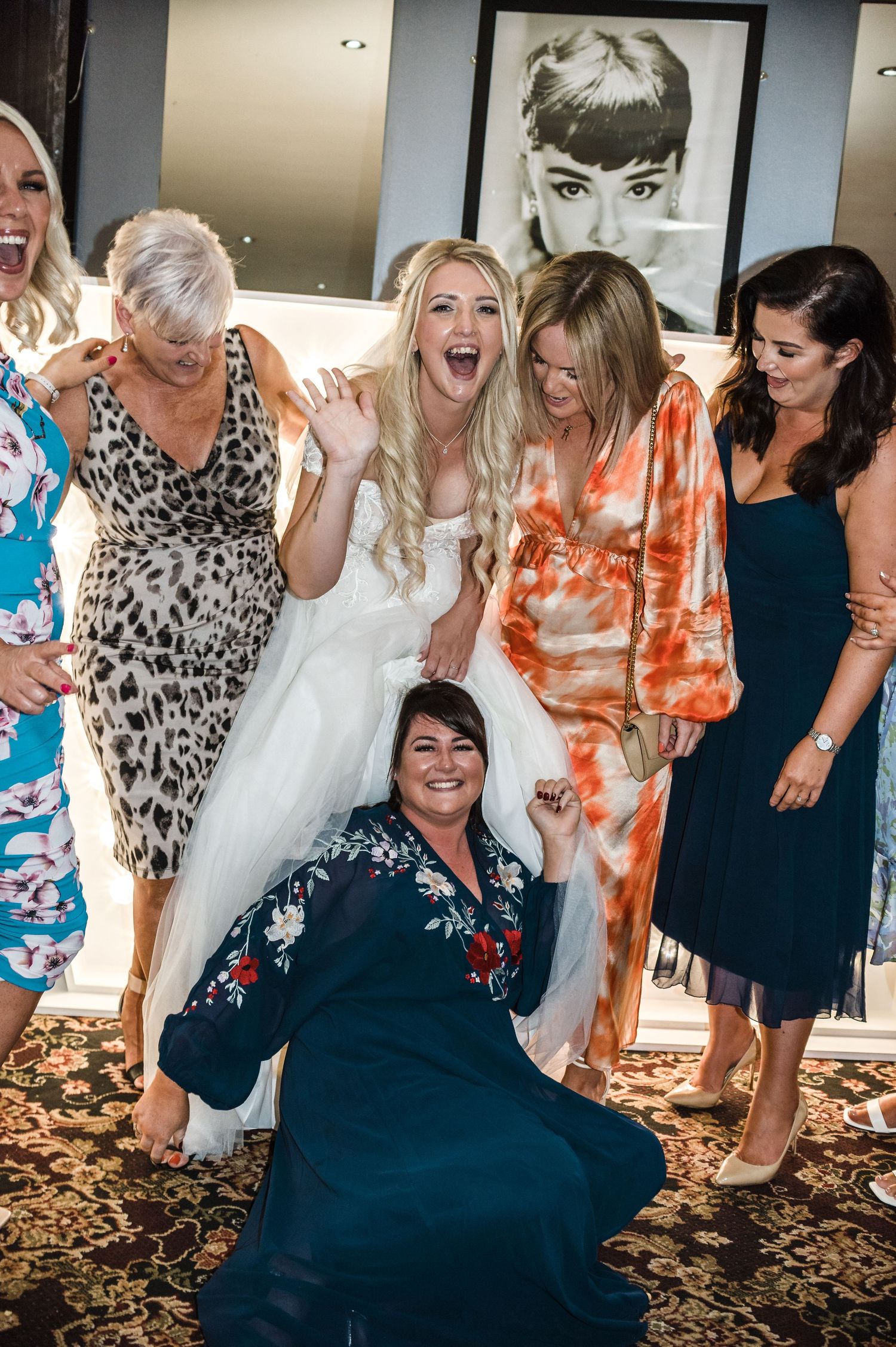 Wedding party celebrates with laughter and joy in front of vintage portrait wall decor.