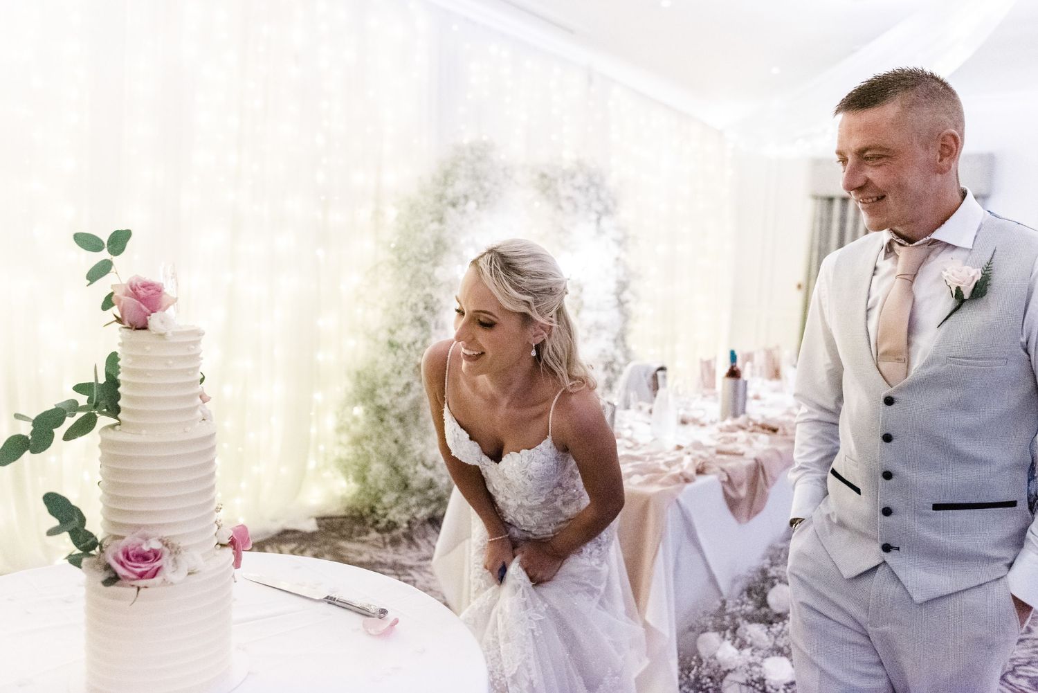 Wedding couple cuts their minimalist white tiered cake in an elegant indoor setting.