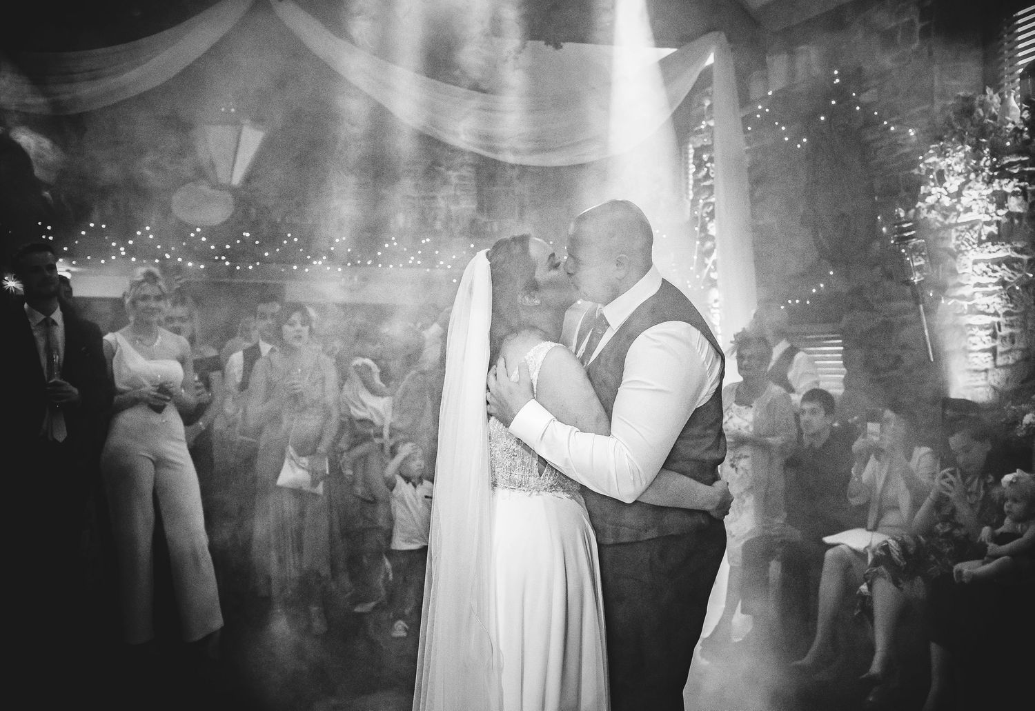 A romantic first dance at a wedding reception with twinkling lights and guests in the background.