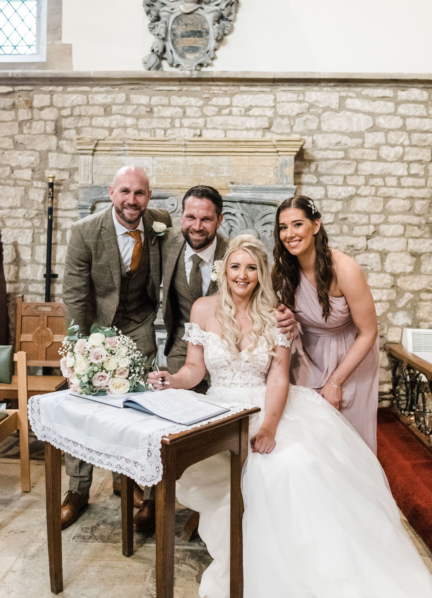 Wedding party gathered around signing table in stone church interior.