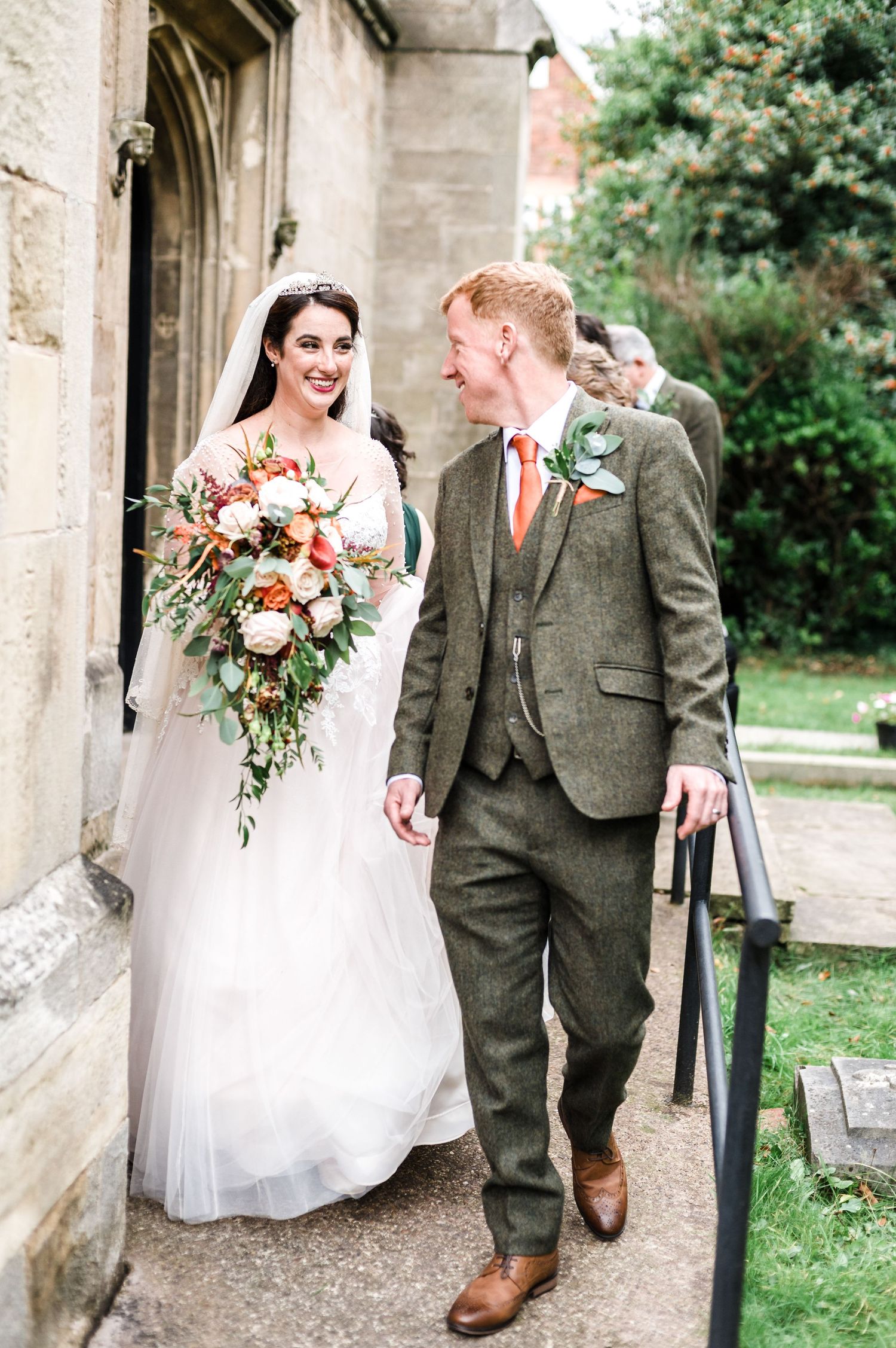 A couple walks along a stone church path during their wedding celebration.