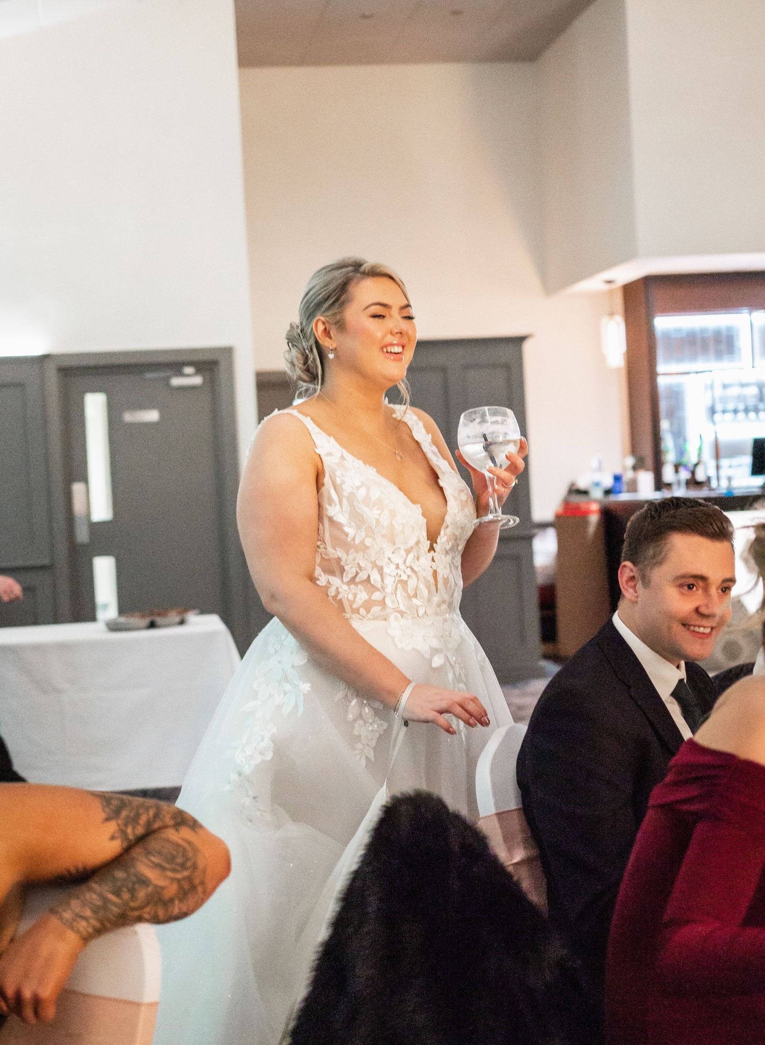 Joyful person in a lace wedding dress holding a champagne glass during a reception celebration.