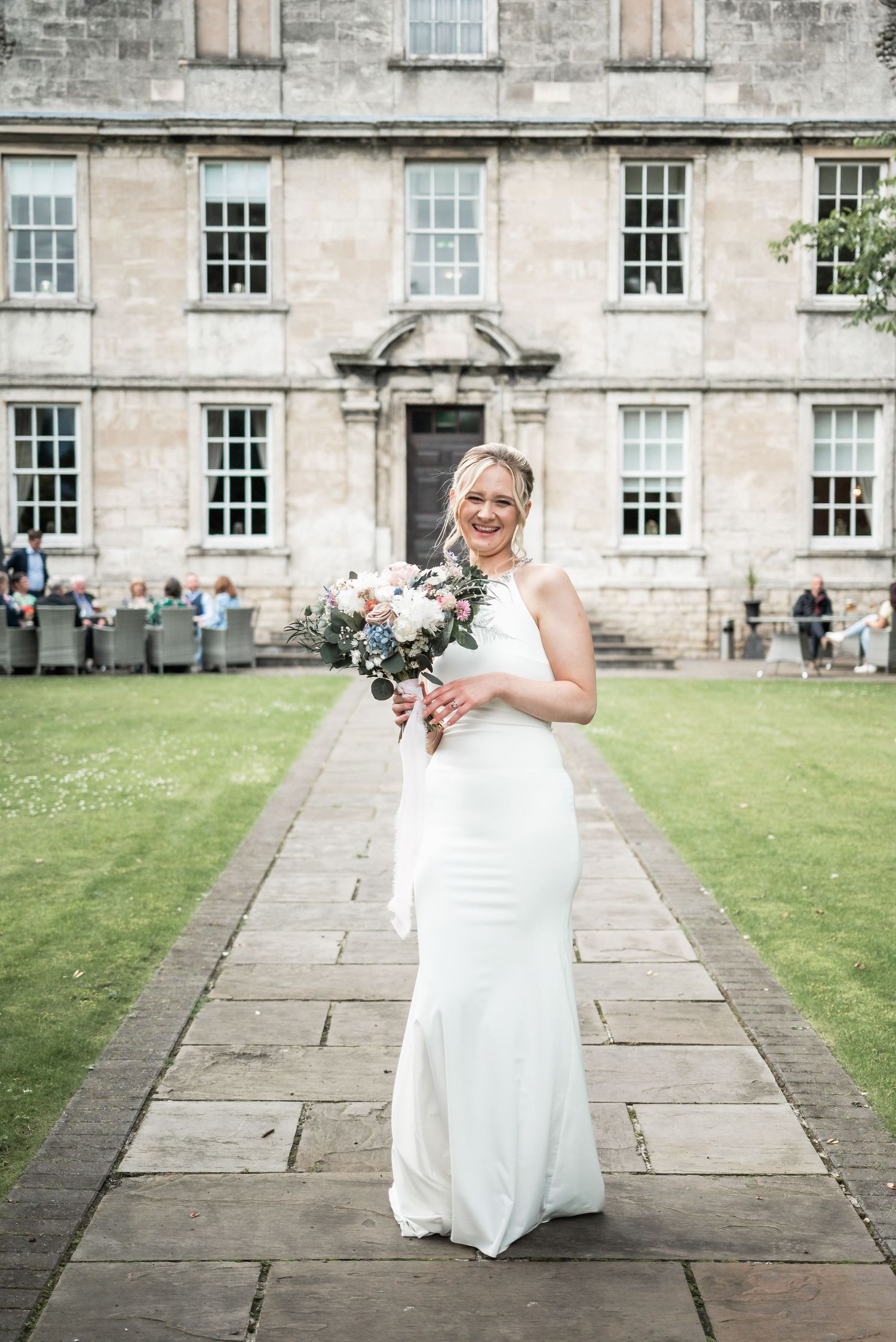 Elegant bride standing on stone path in front of historic mansion with beautiful bouquet.