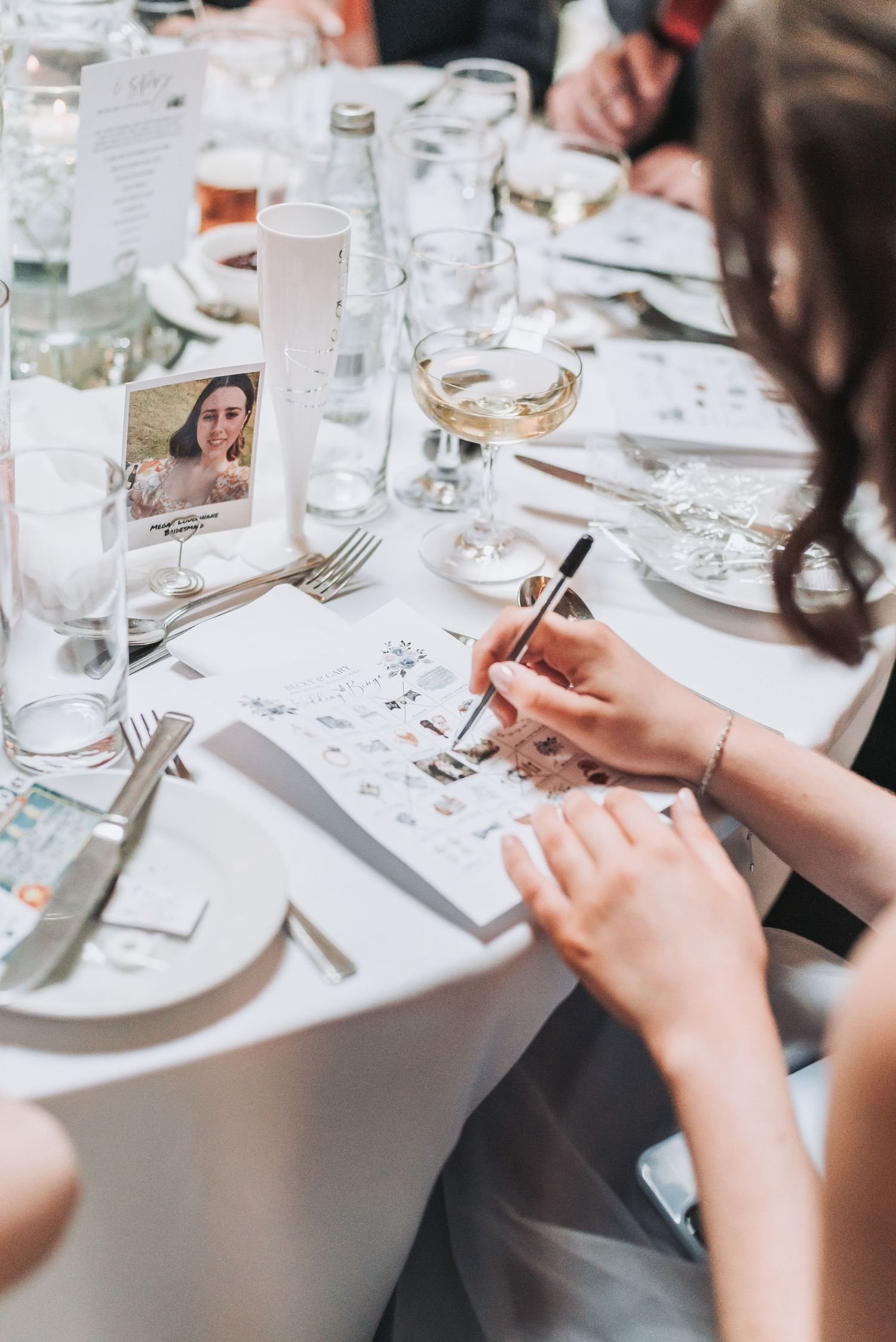 Wedding reception details showing place settings and handwritten notes on a white tablecloth.