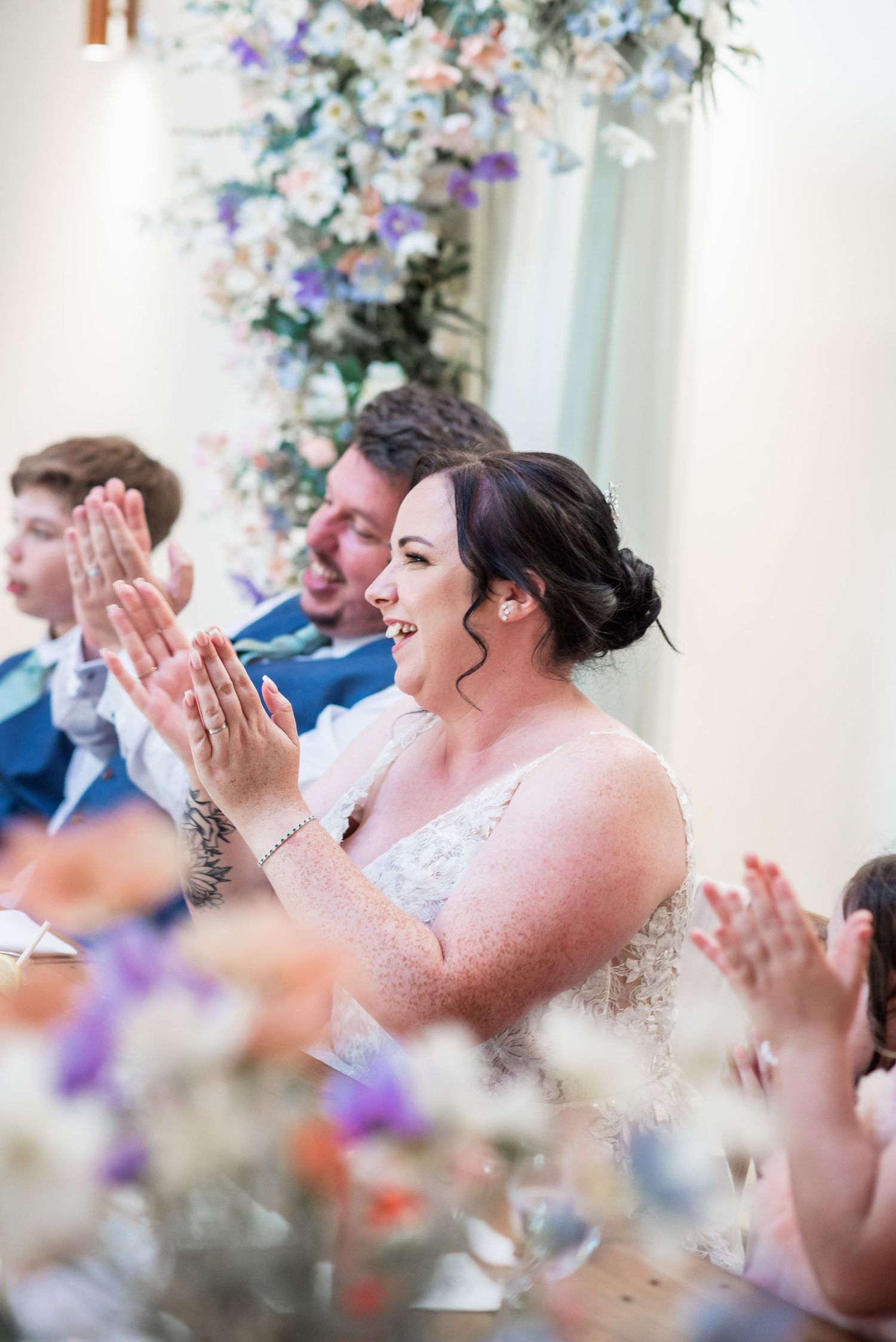 Wedding reception scene with floral arrangements and applauding guests.