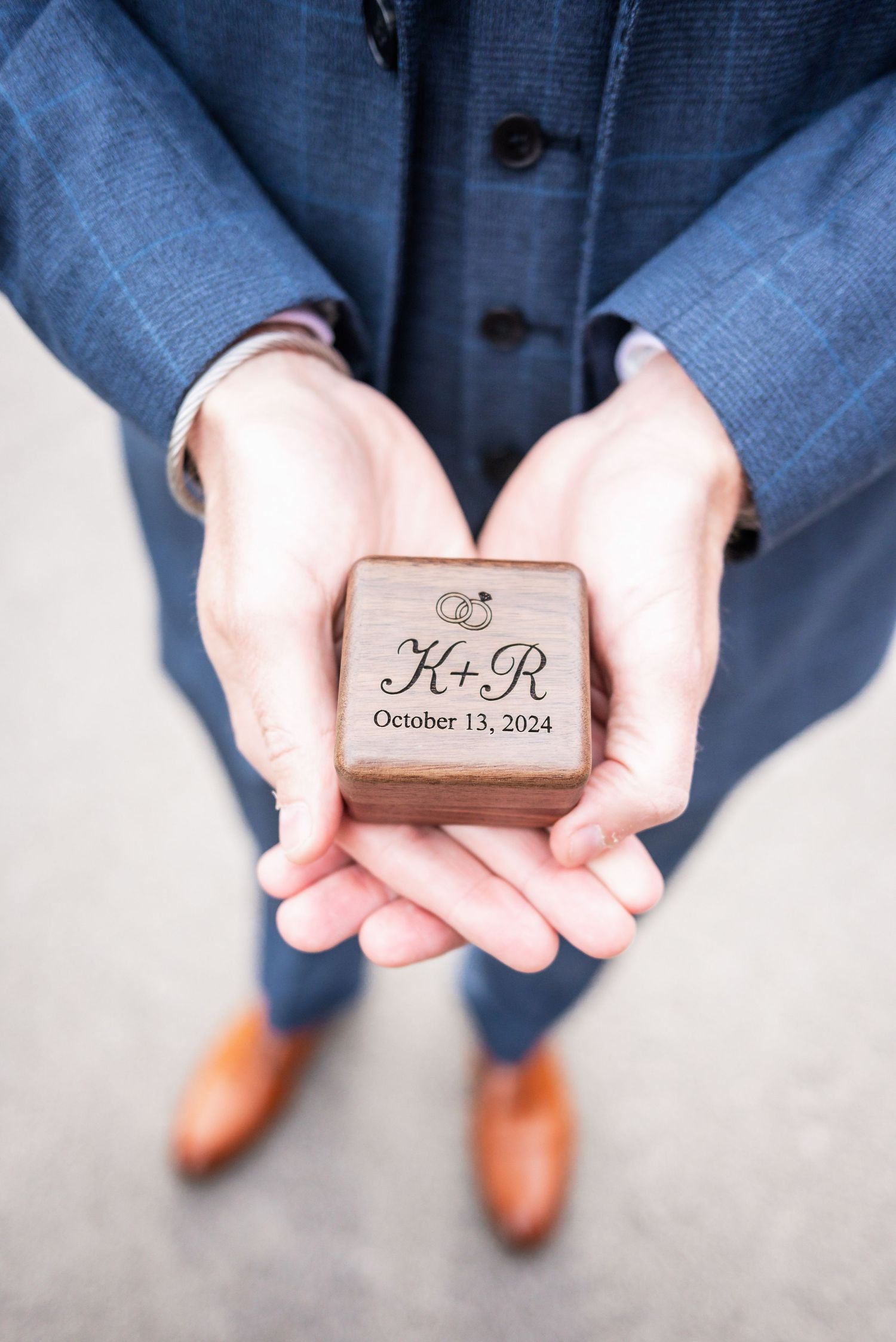 Close-up of hands holding wooden ring box with October 13, 2024 wedding date engraved.