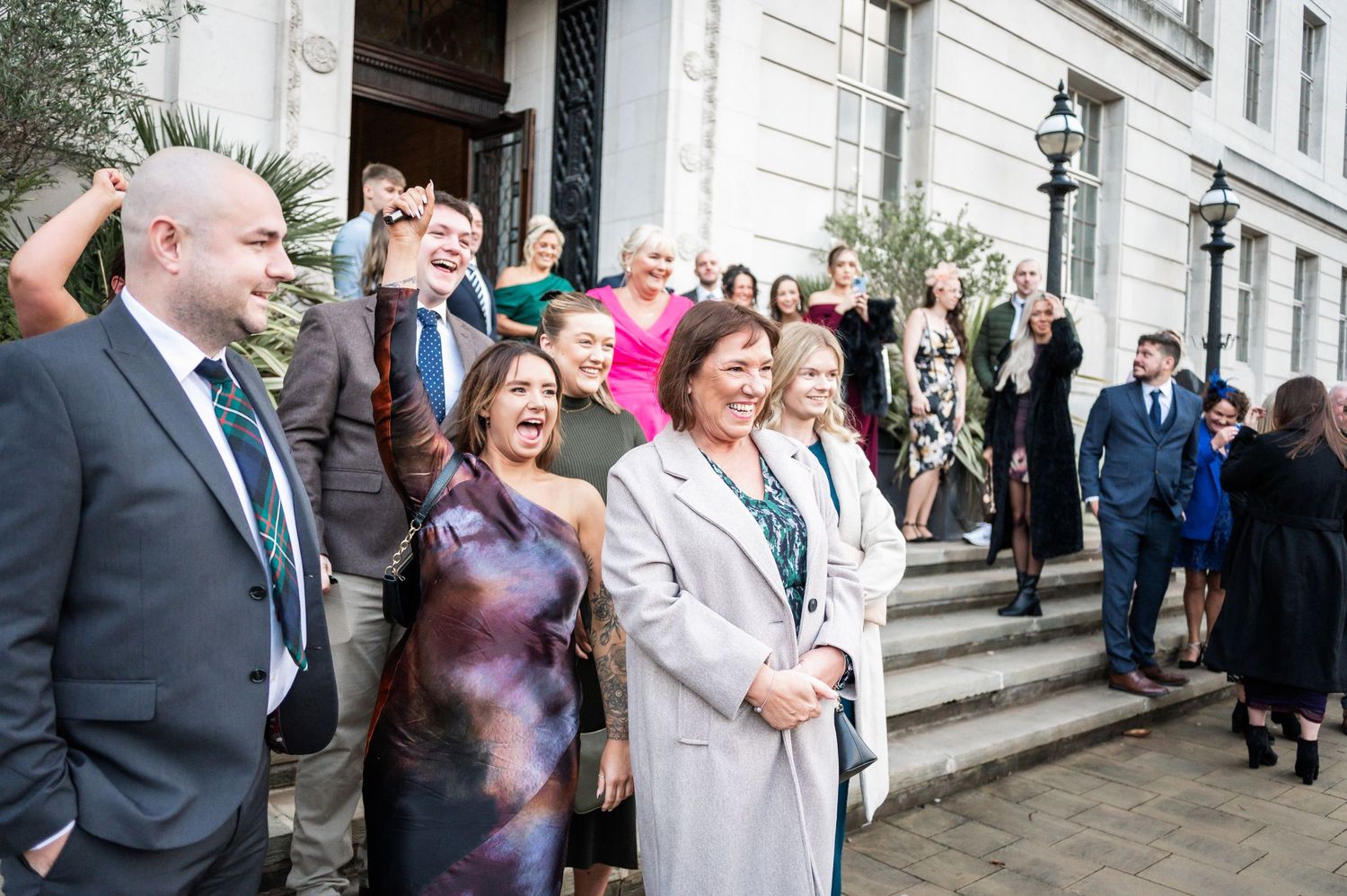 Wedding guests gathered on stone steps share laughter during celebration.