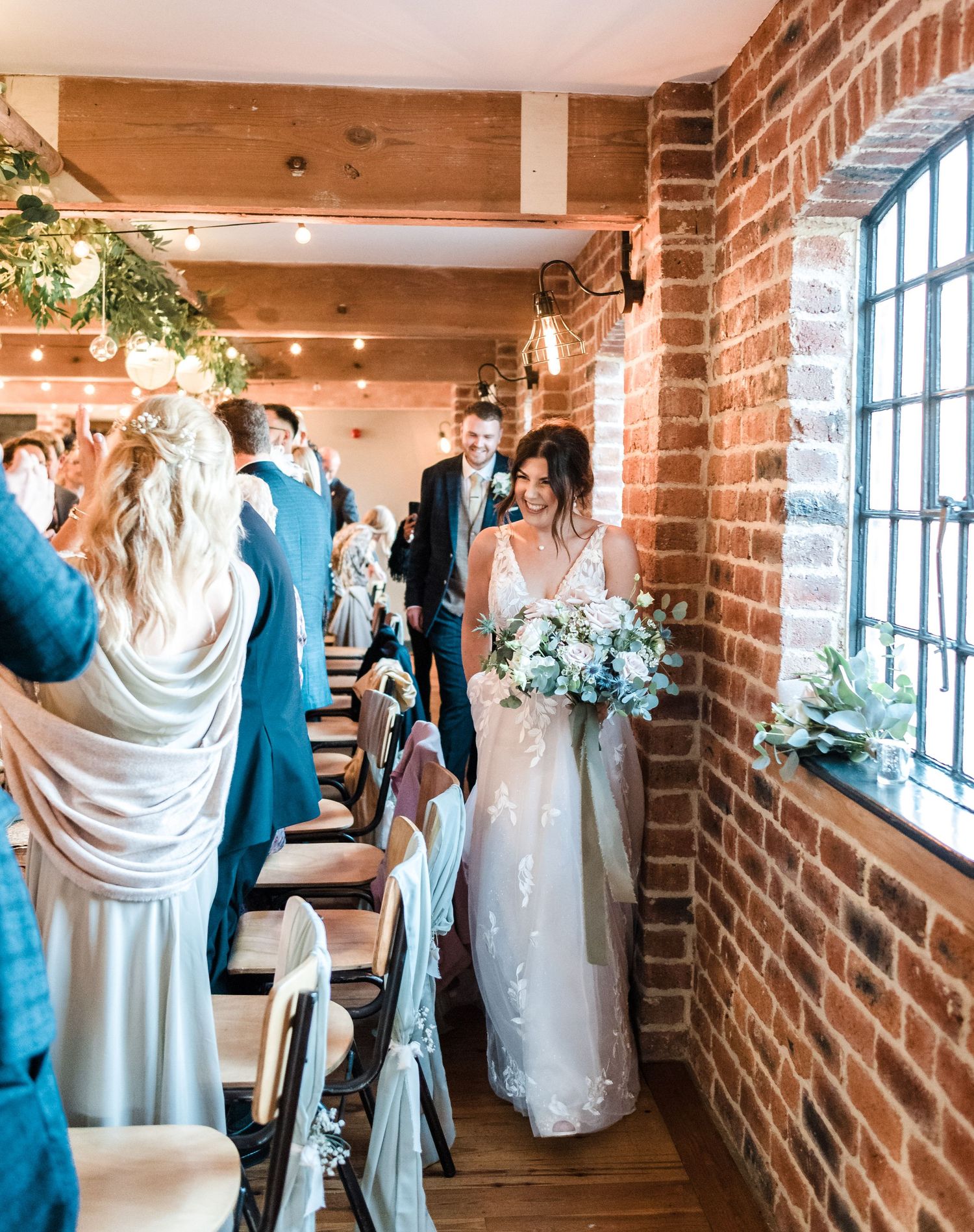 Wedding ceremony processional in rustic brick venue with white floral arrangements.