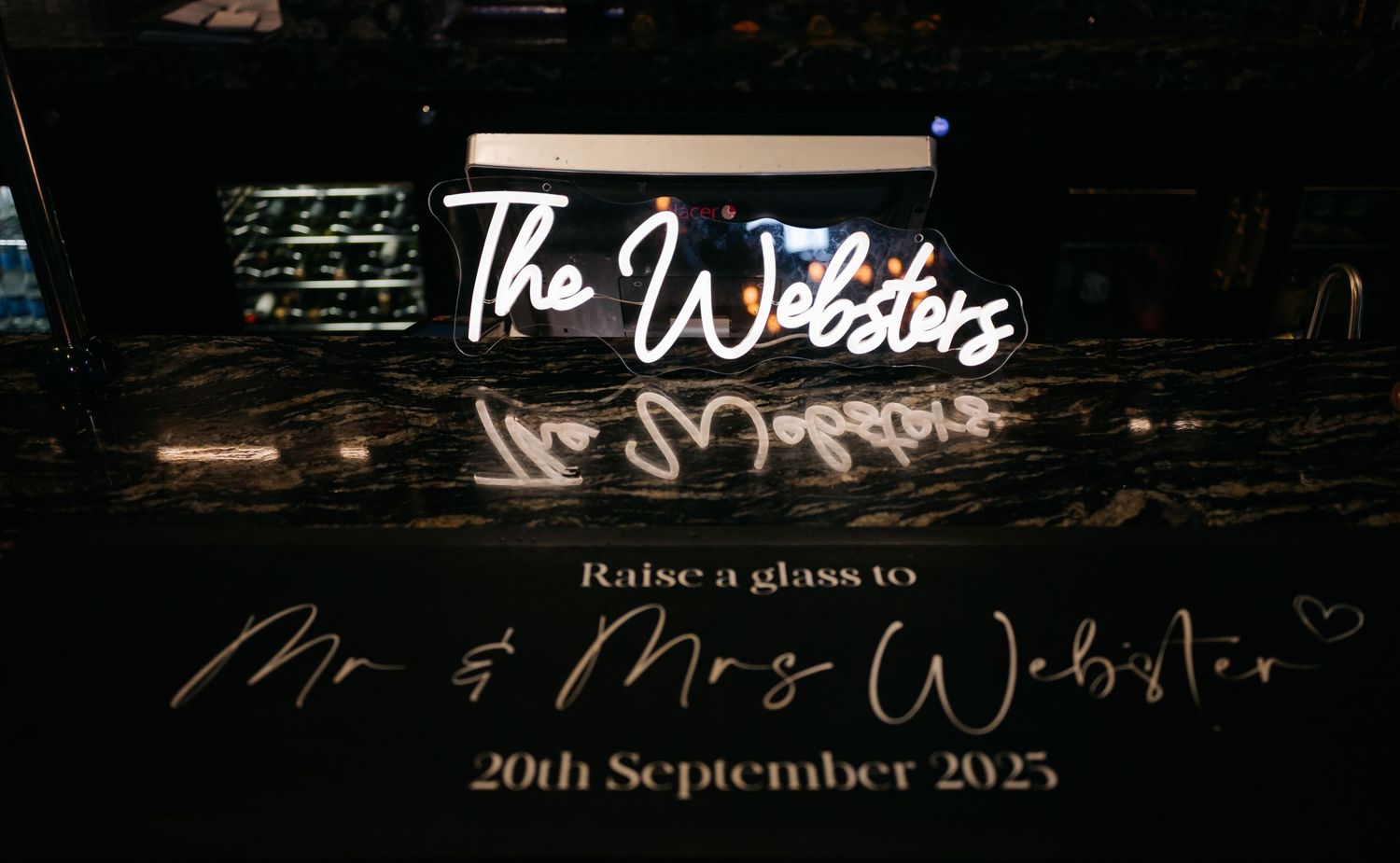 Dark reception venue with illuminated wedding signage and decorative lighting creating an elegant atmosphere.