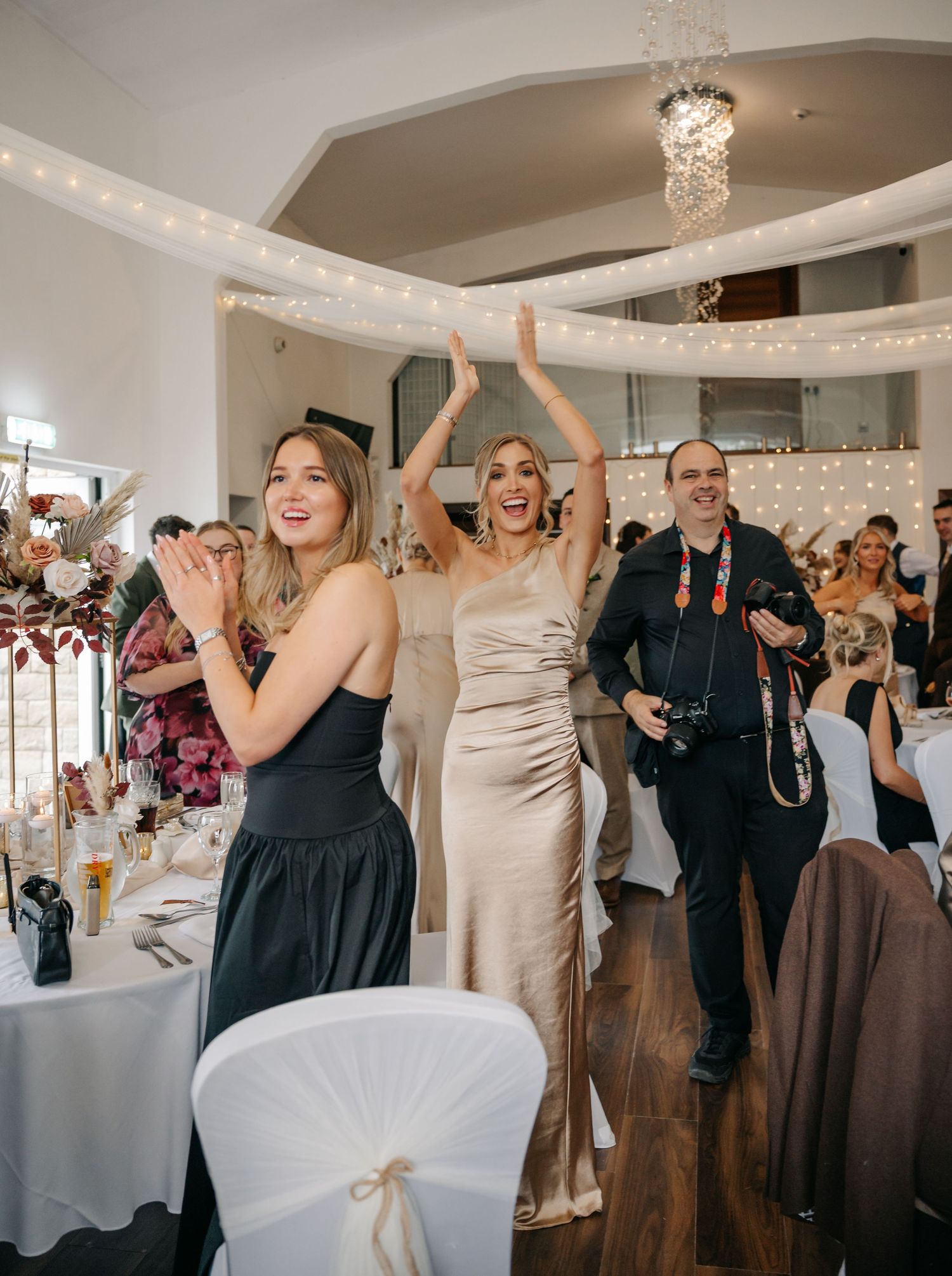 Wedding reception celebration with guests dancing under crystal chandeliers and string lights.