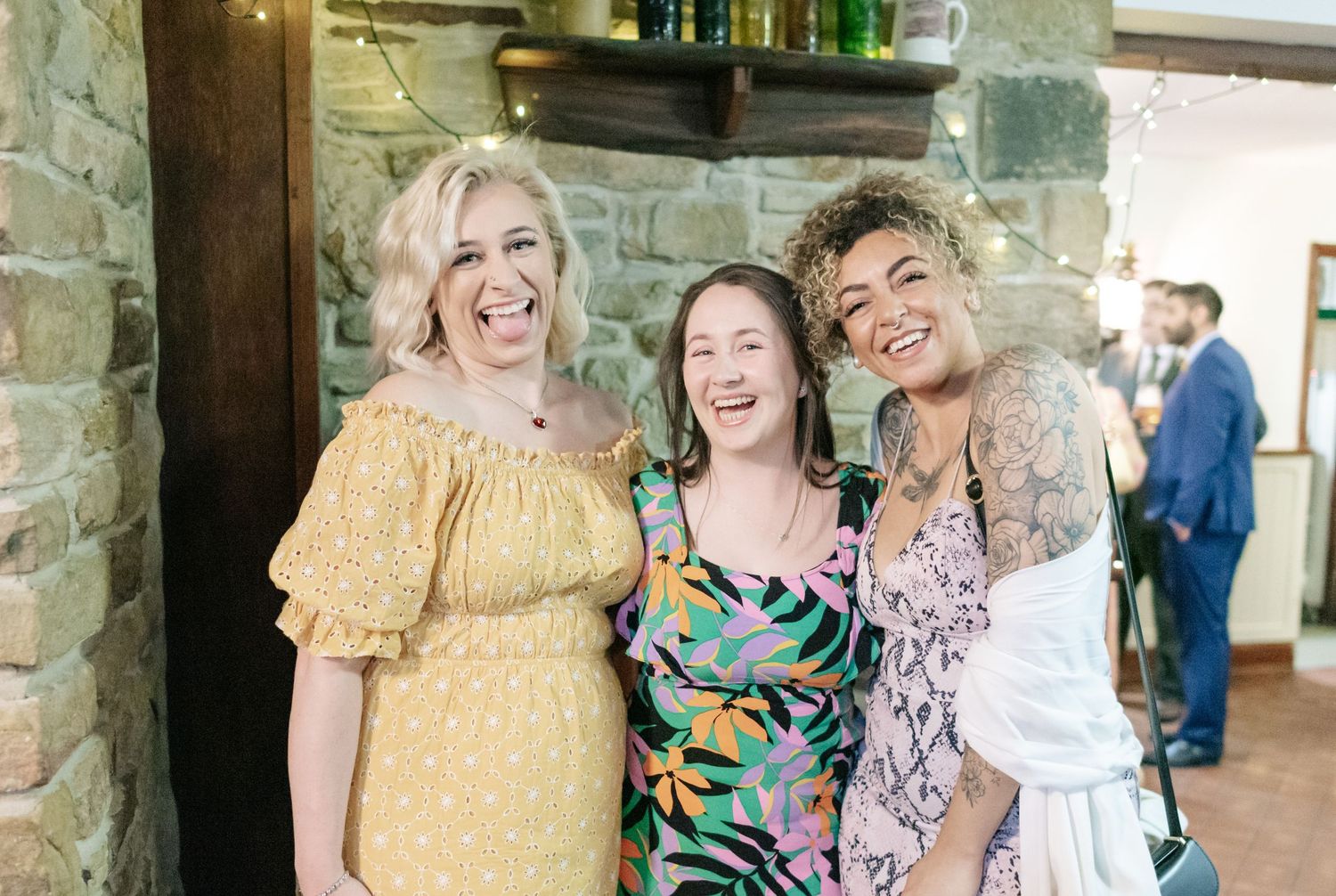 Wedding party members share joyful moments and laughter together in an indoor venue with stone walls.
