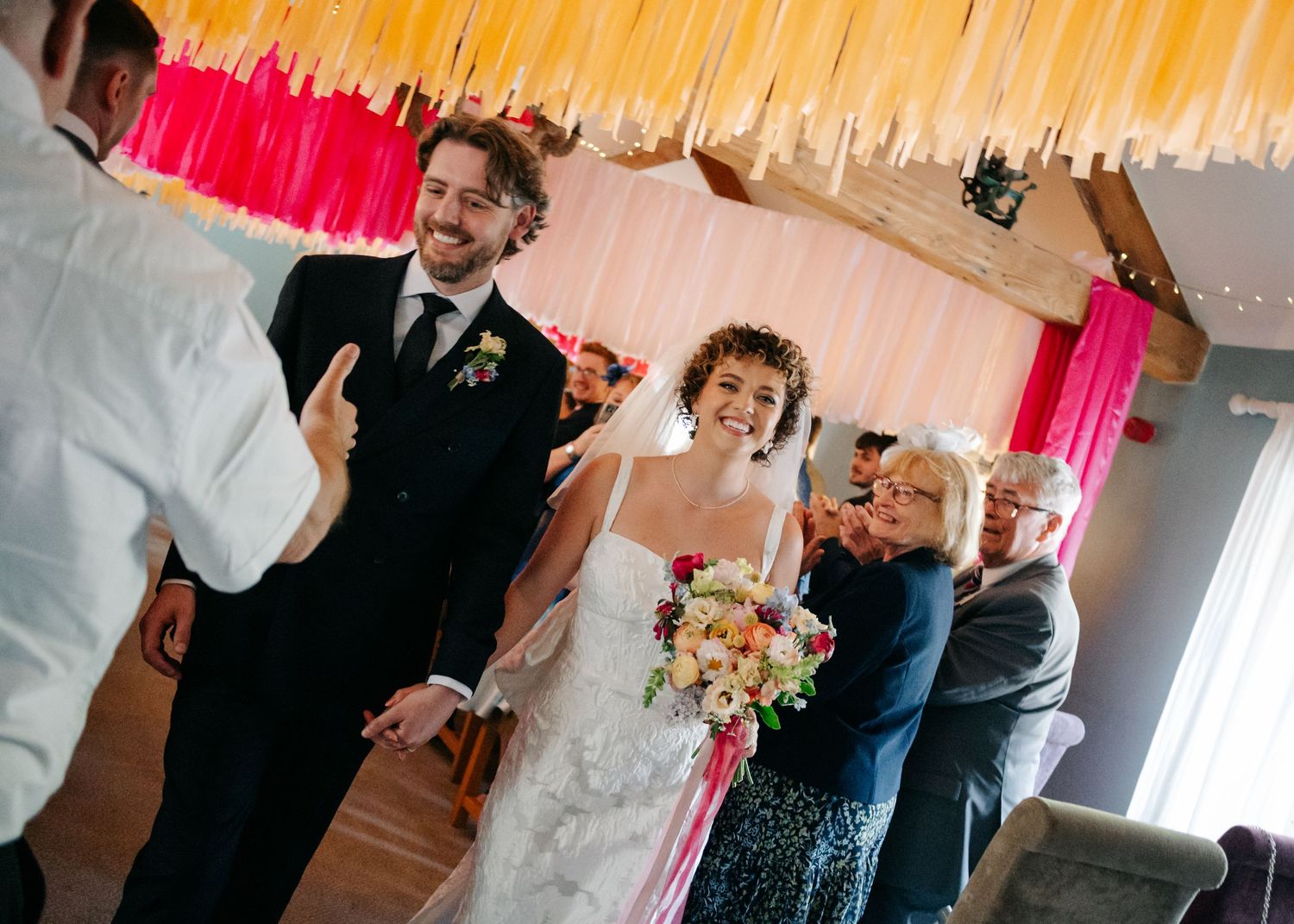 Wedding celebration in a venue decorated with colorful hanging streamers and ambient lighting.
