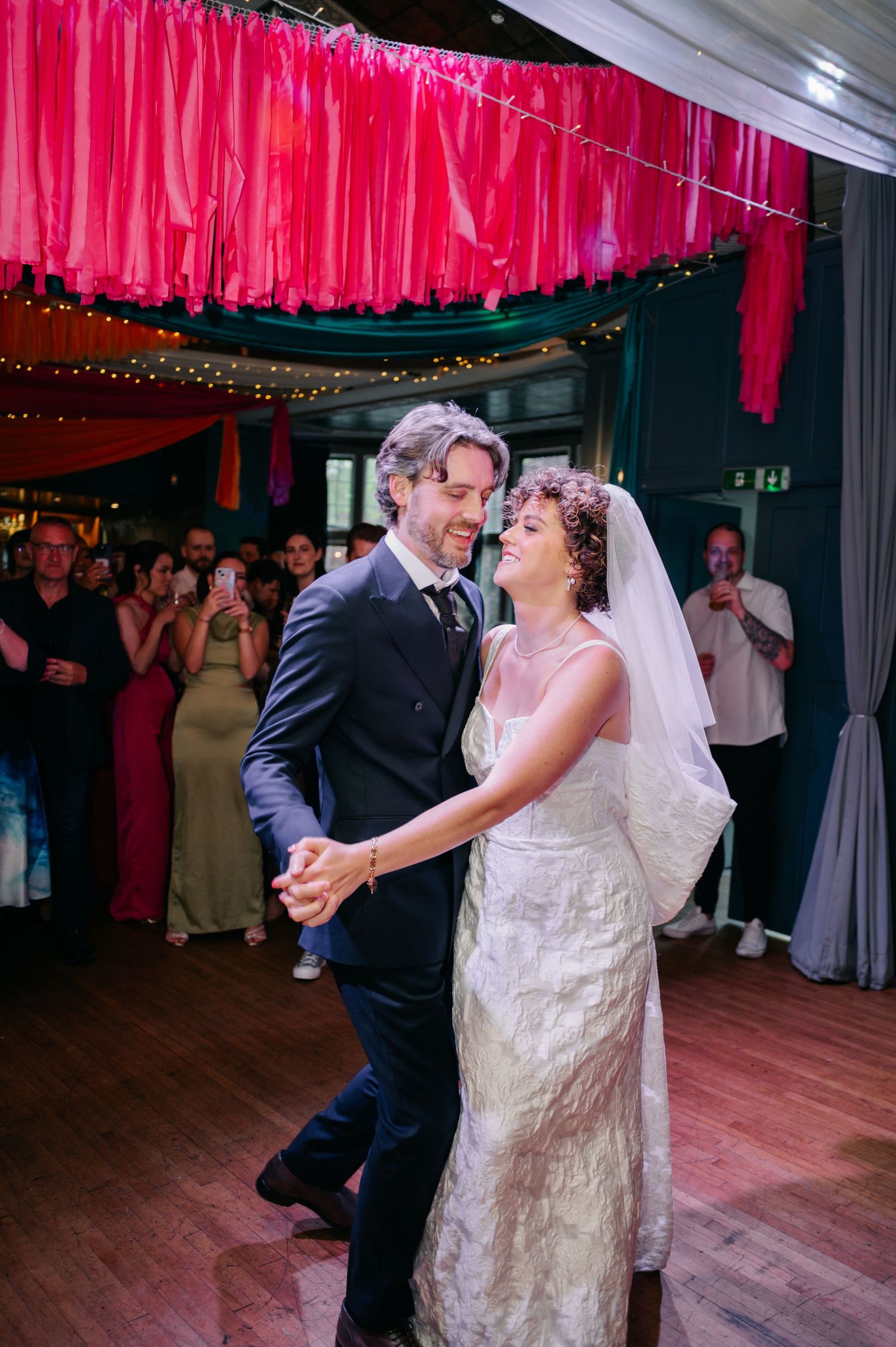 First dance moment under pink fabric draping and twinkle lights at wedding reception.