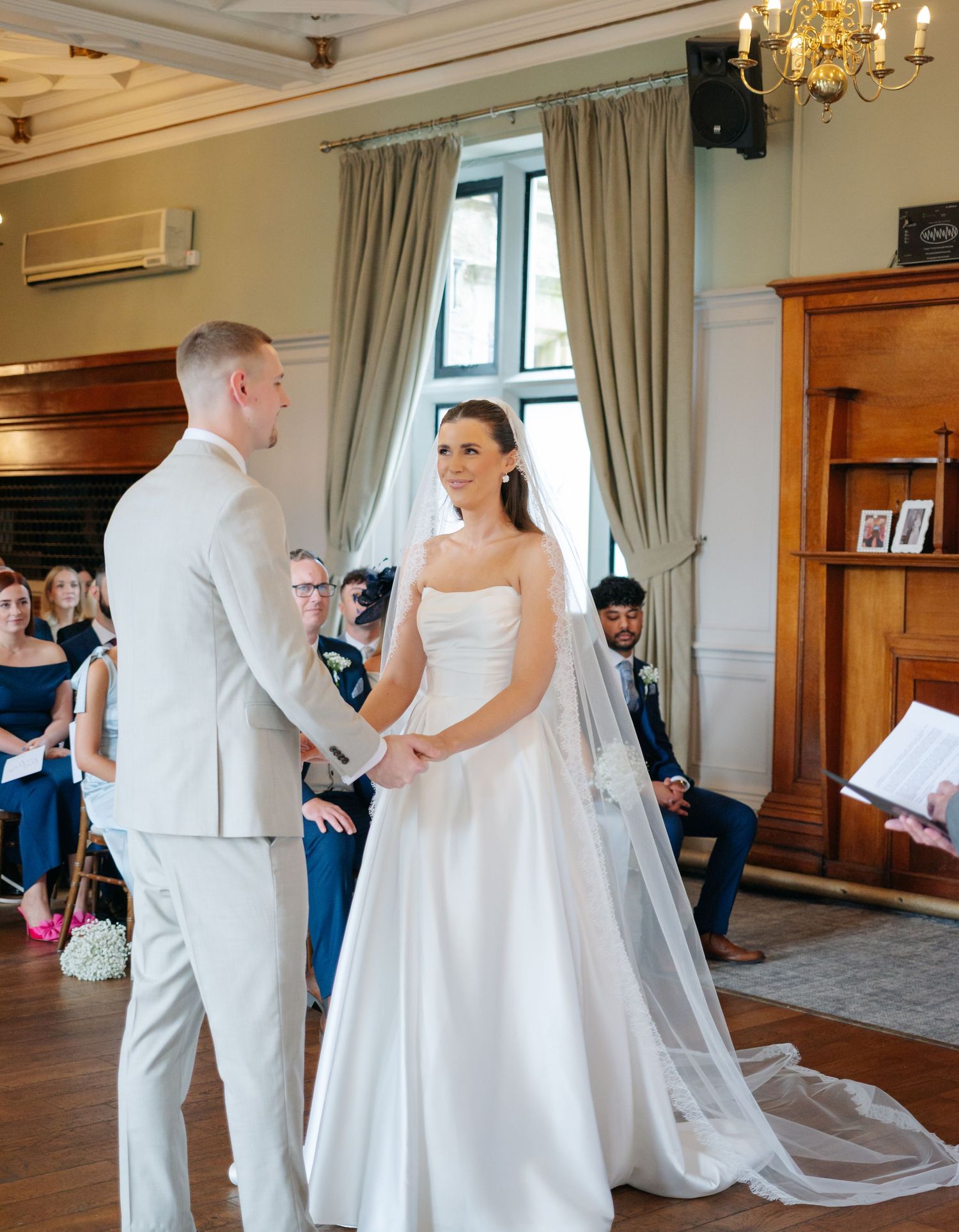 Wedding ceremony in an elegant room with chandelier and wooden panels.