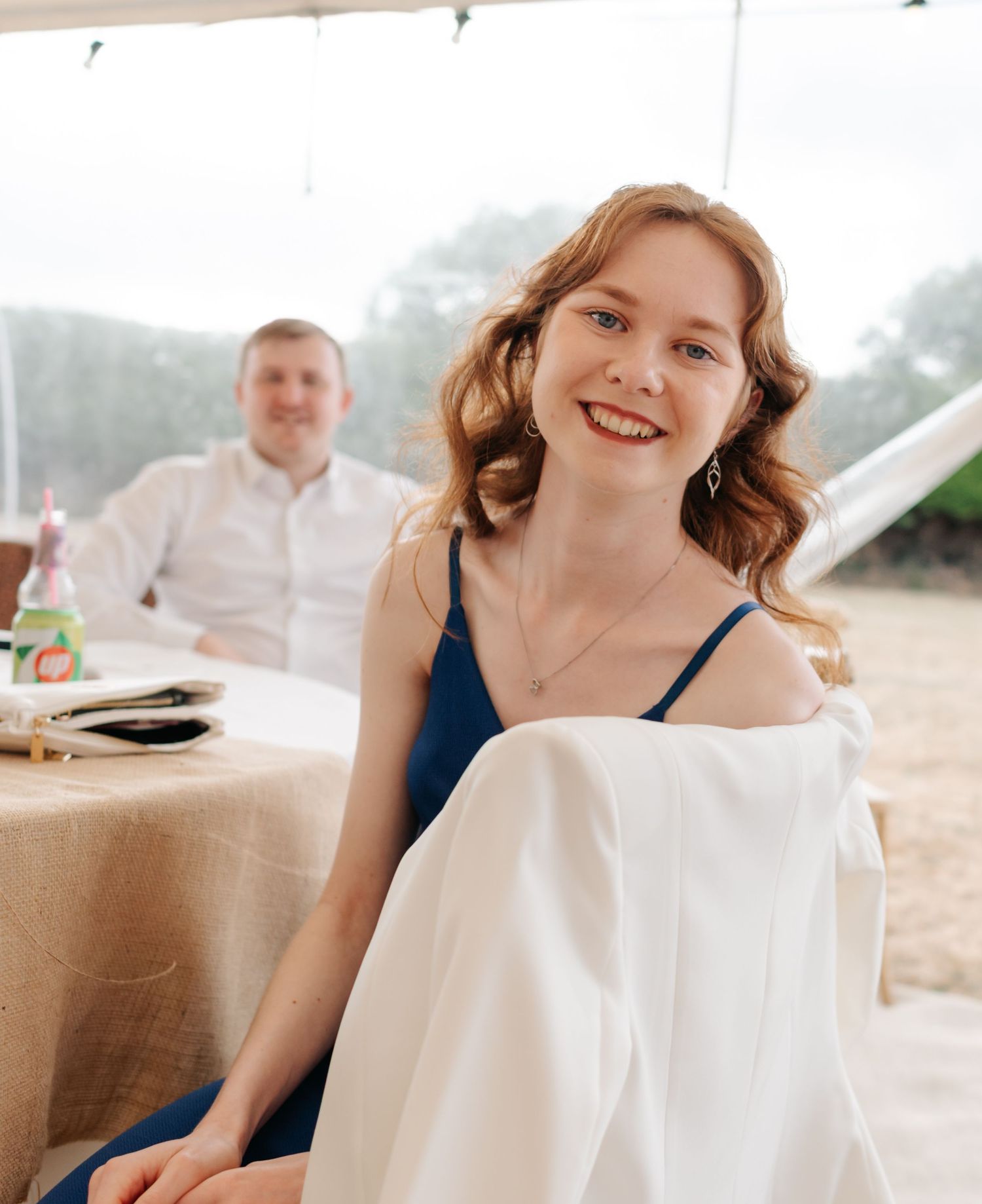 Wedding reception guests enjoy casual moments on hay bales under white tent.