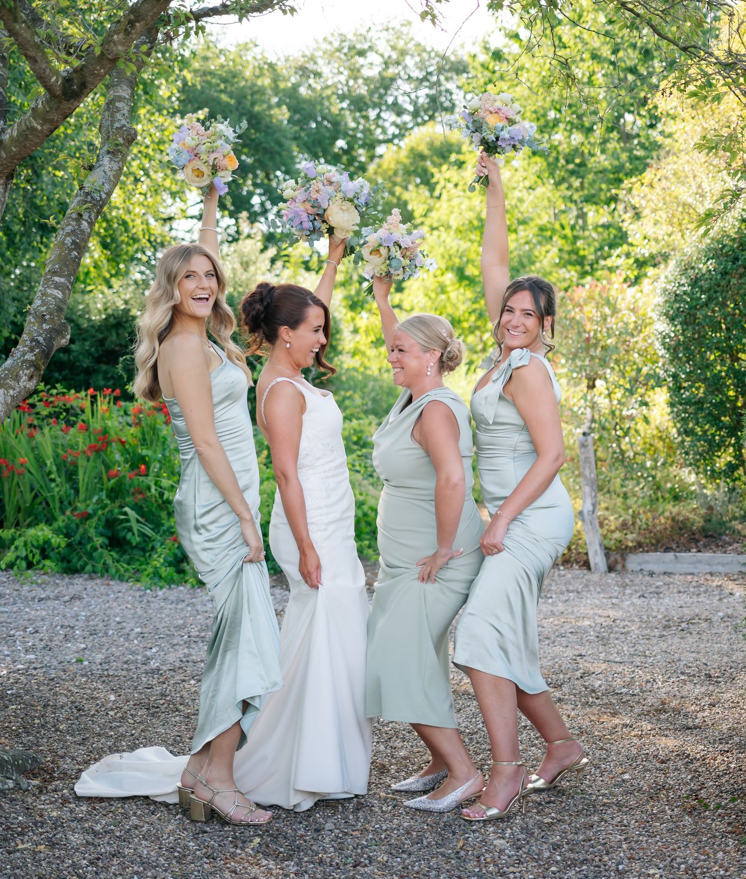 Bridesmaids in light mint dresses posing playfully on gravel path.