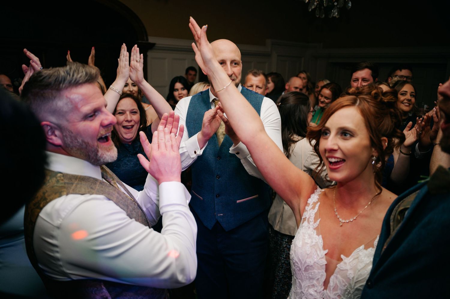 Wedding party dancing and celebrating in a dimly lit reception venue.