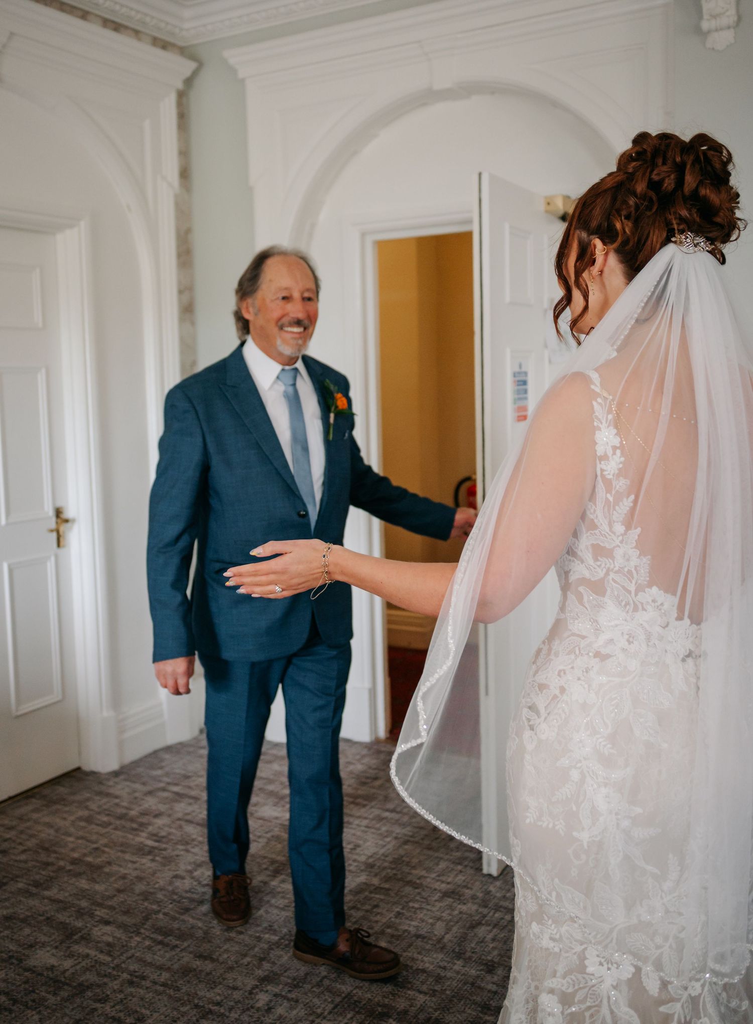 A first look moment between a bride in white lace and person in a navy suit before the wedding ceremony.