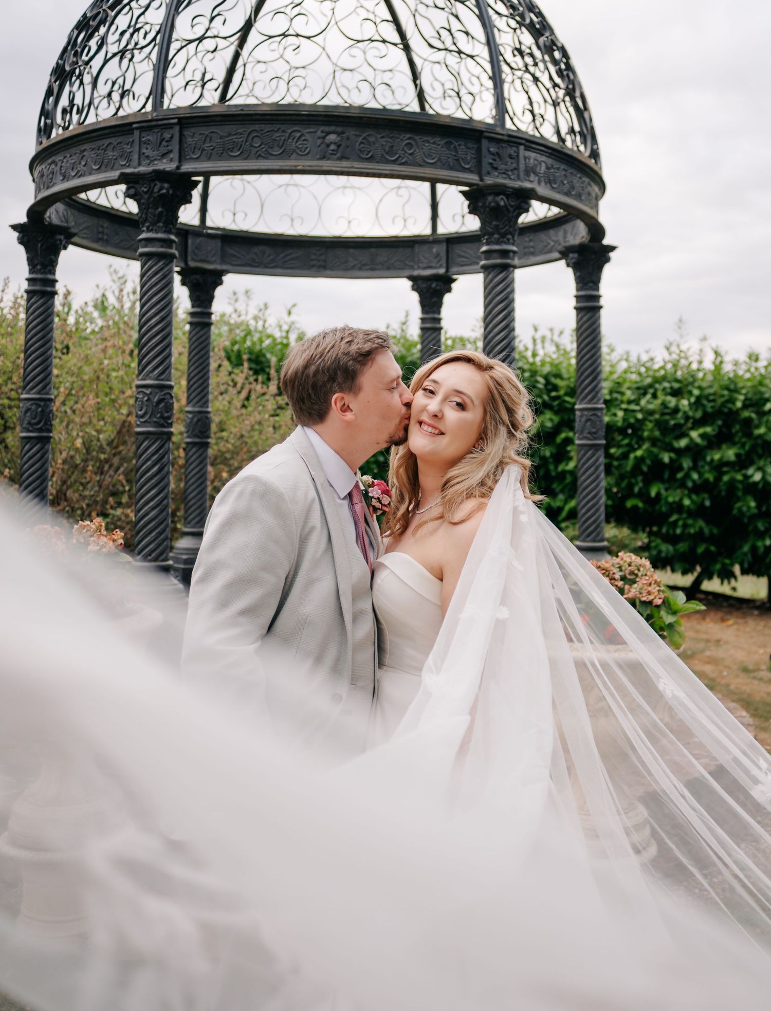A romantic moment captured under an ornate metal gazebo with flowing white veil.