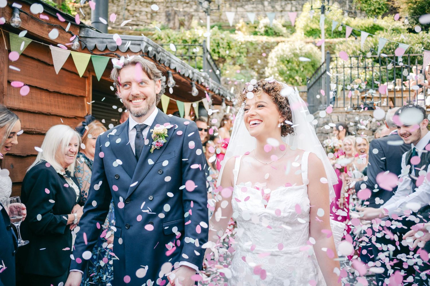 Wedding party celebrating outside with confetti throwing in a garden setting.