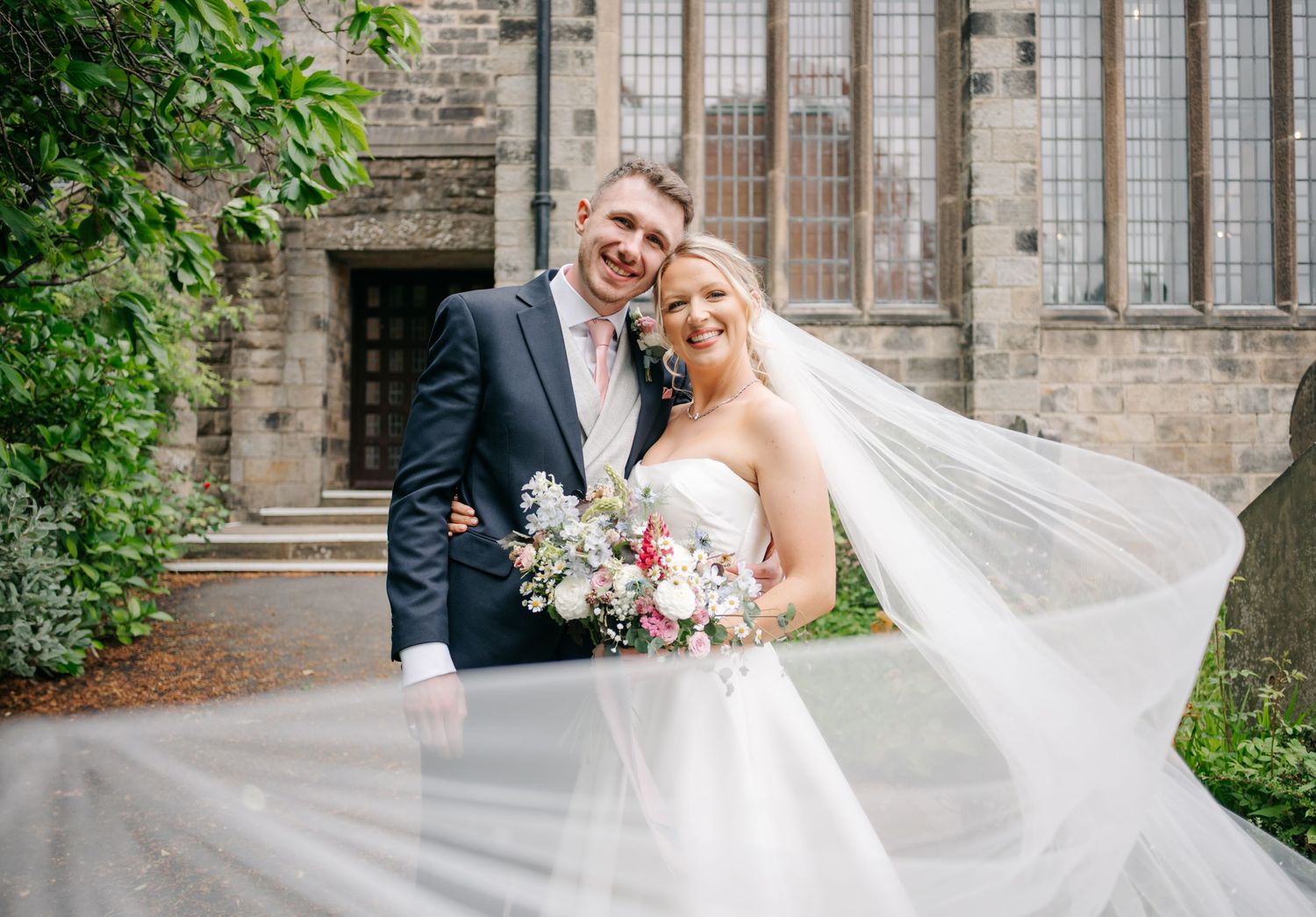 Elegant wedding portraits taken outside historic stone church with gothic windows.