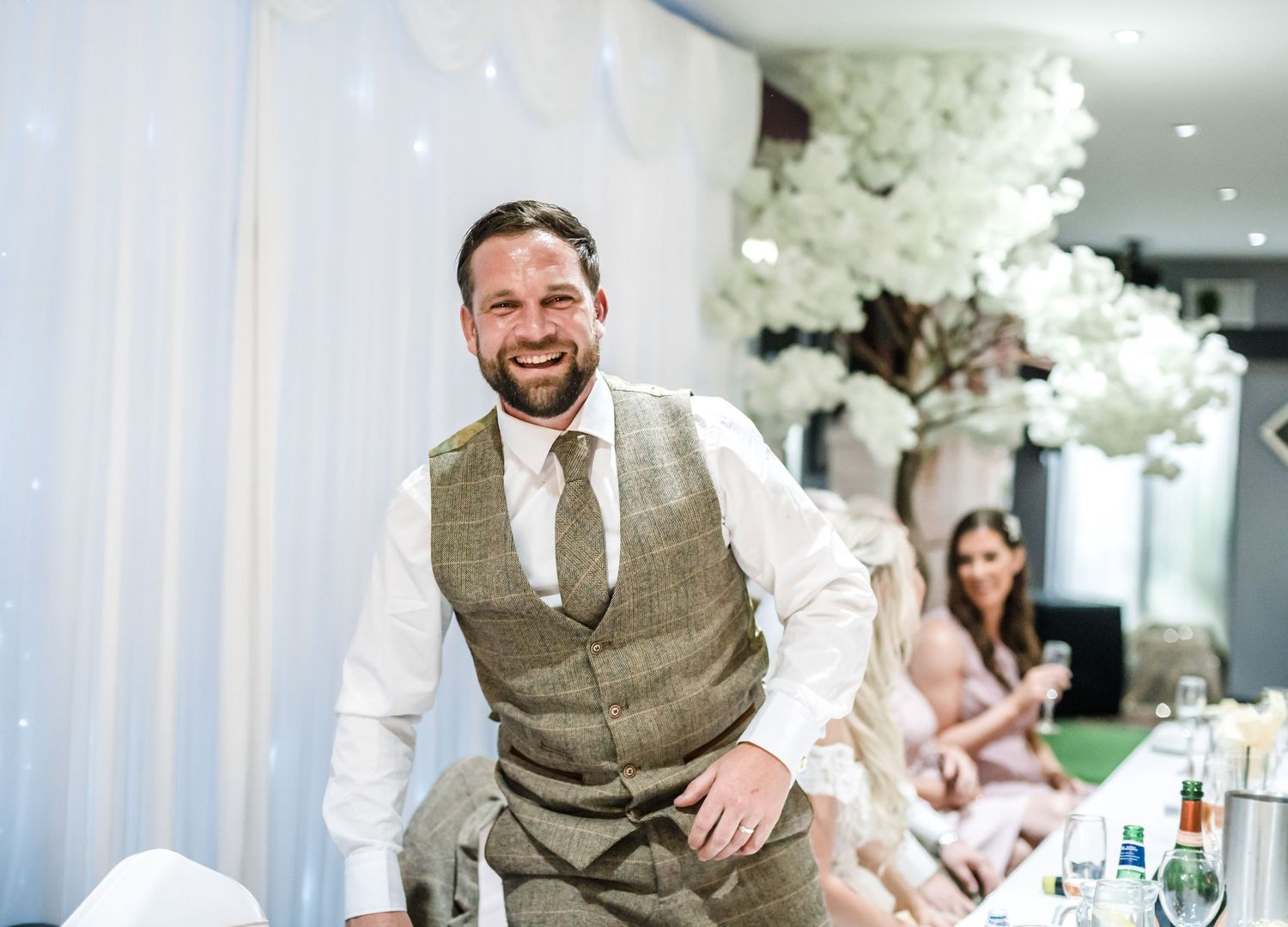 A wedding reception scene with tables set for dinner and elegant white floral decorations.