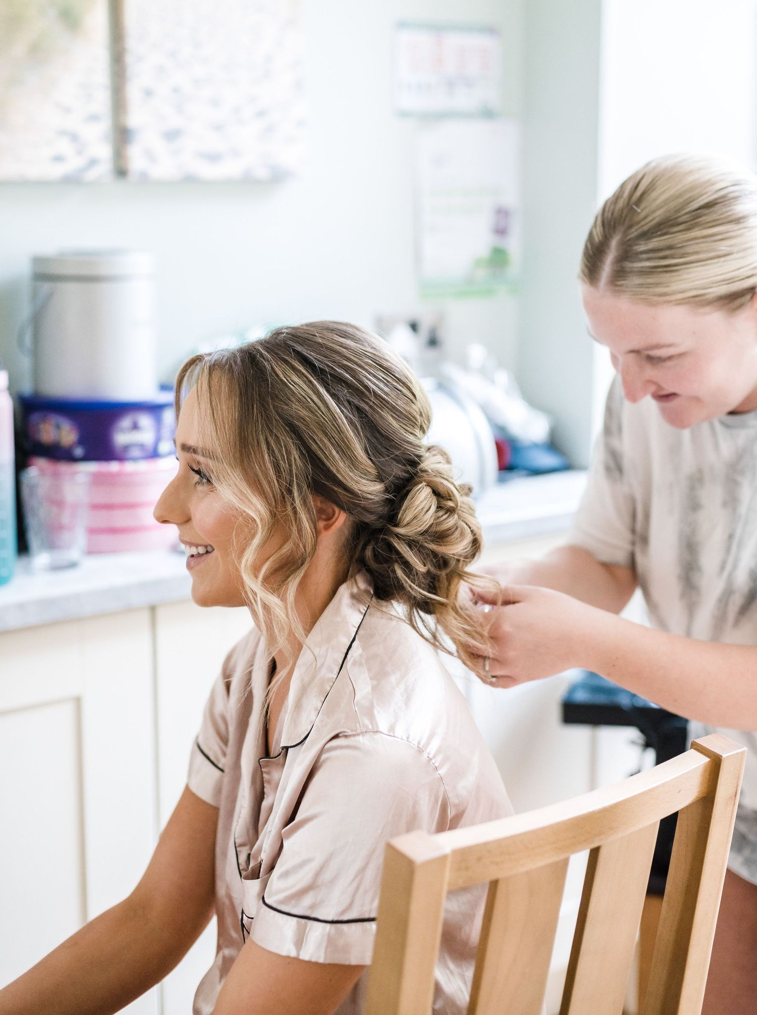 A hairstylist works on styling a bride's hair in a bridal preparation scene.