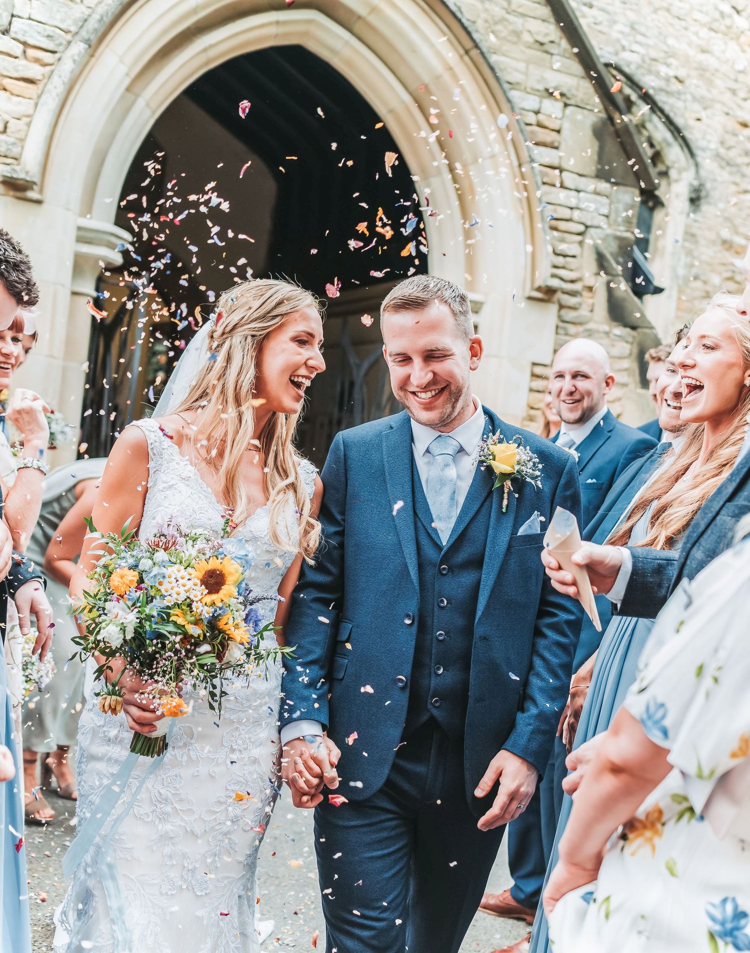 Wedding couple walks through confetti shower outside historic church entrance.
