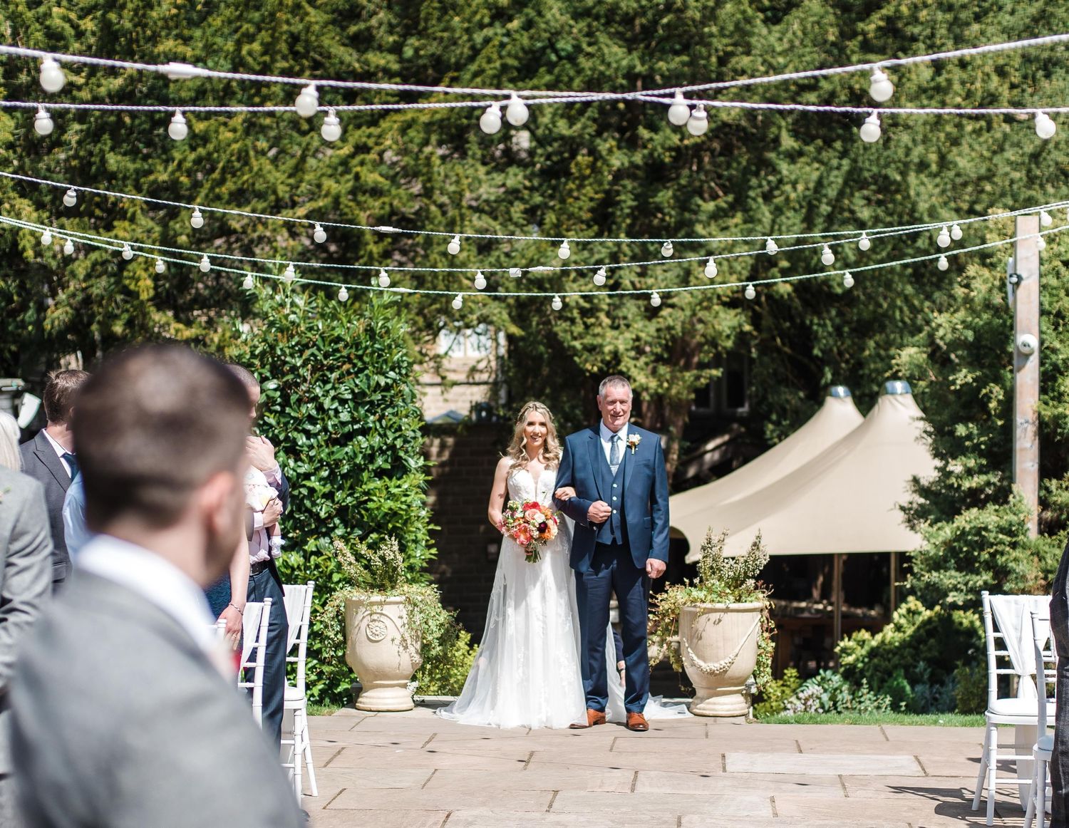Outdoor garden wedding ceremony setup with string lights and guests seated.