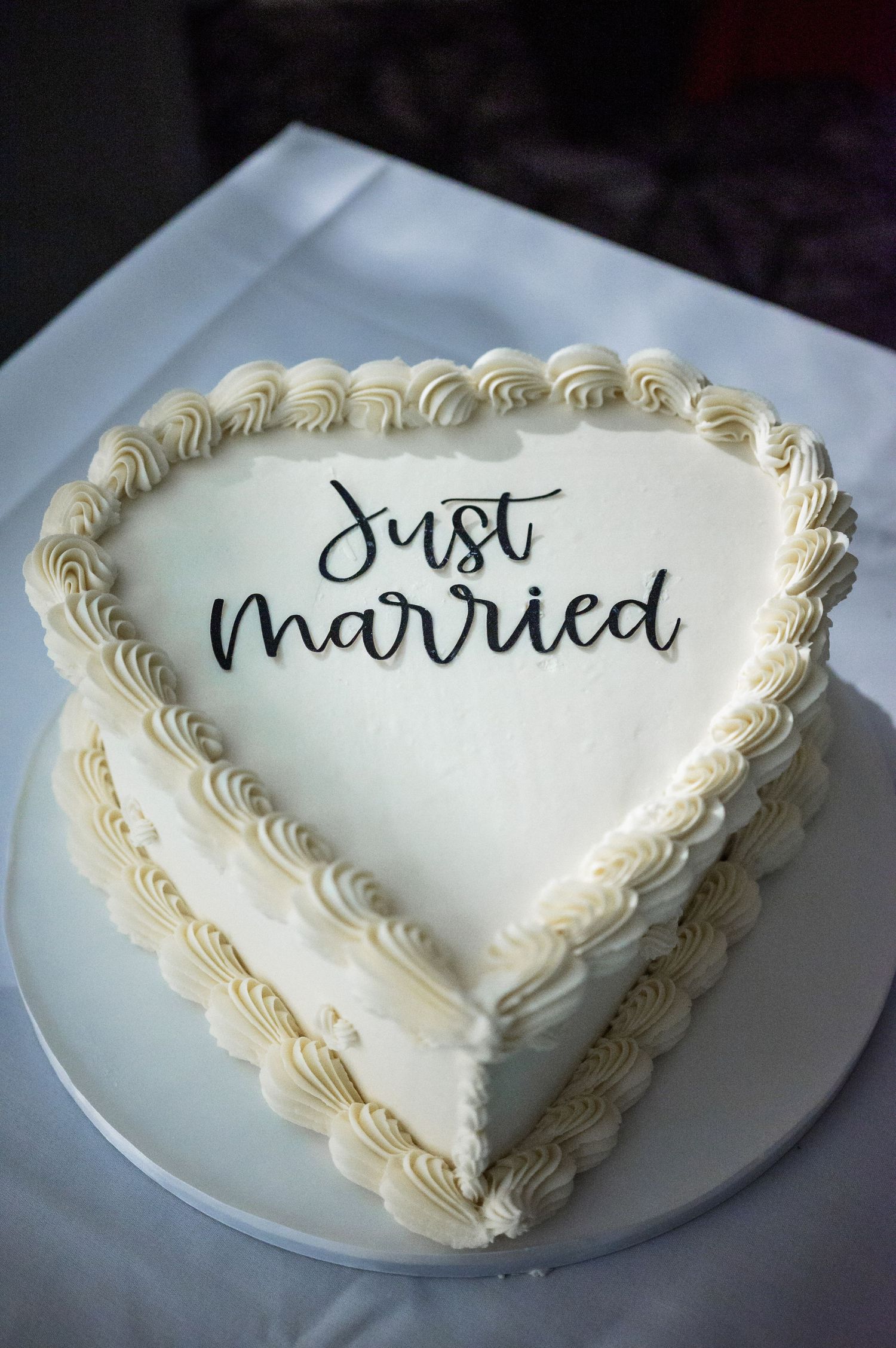 Heart-shaped white wedding cake with 'Just Married' written in elegant black script and piped frosting border.