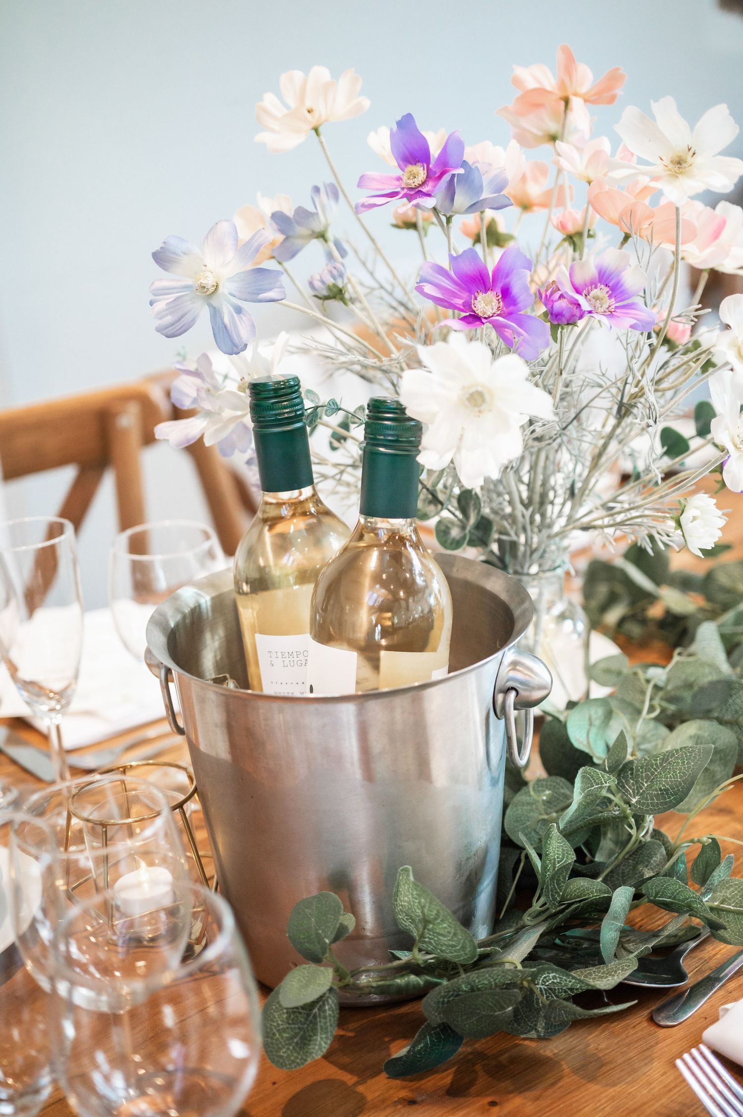 Wine bottles in ice bucket with delicate wildflowers and eucalyptus table decoration.
