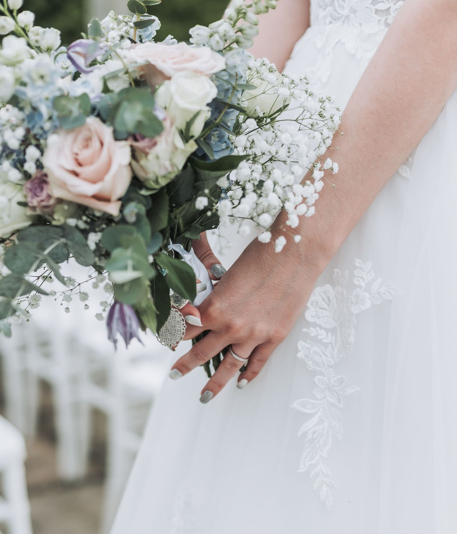 Close-up of bridal bouquet featuring pink roses, baby's breath, and eucalyptus with lace dress details.