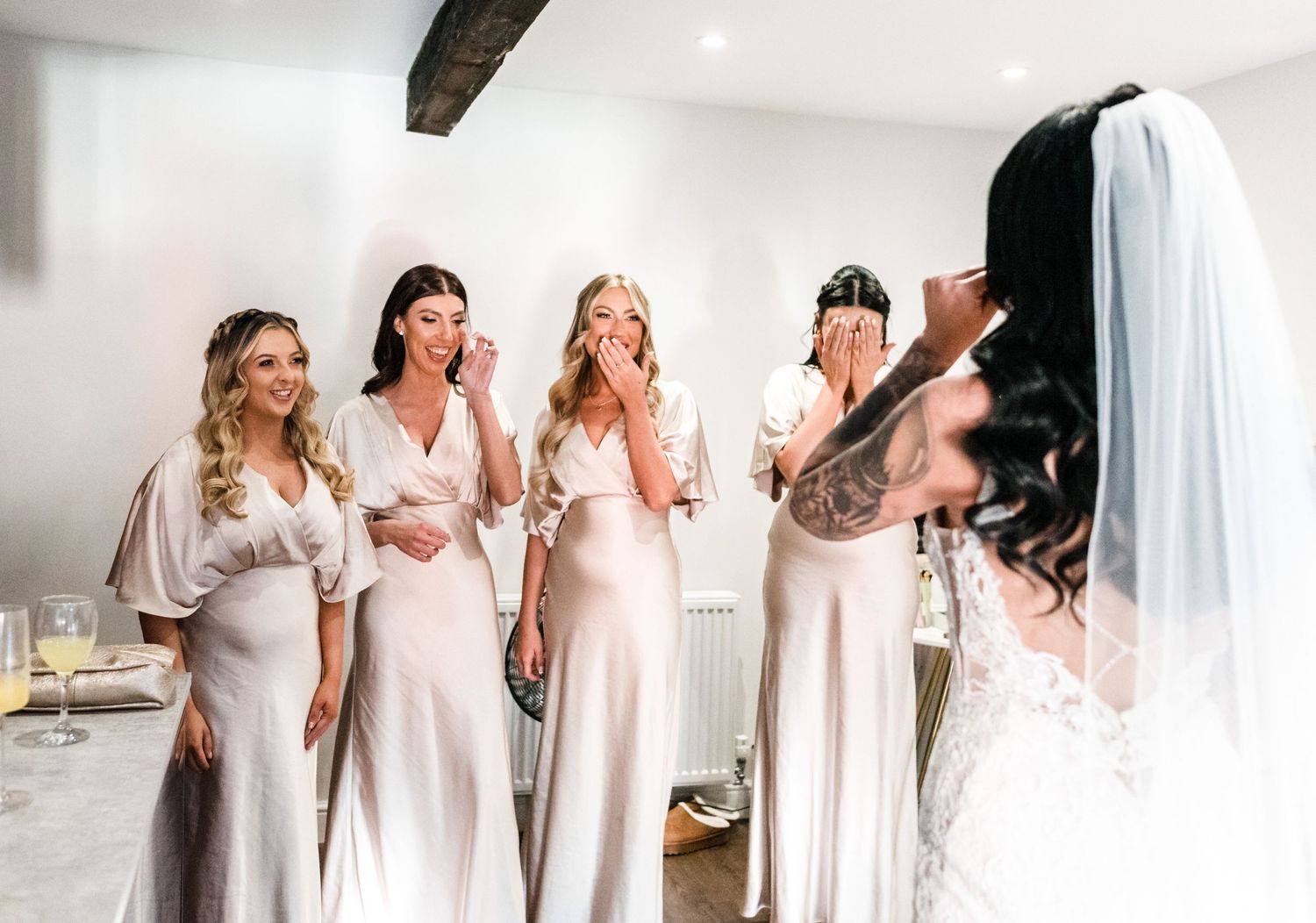 Bridesmaids in light colored dresses react with excitement during wedding preparations.