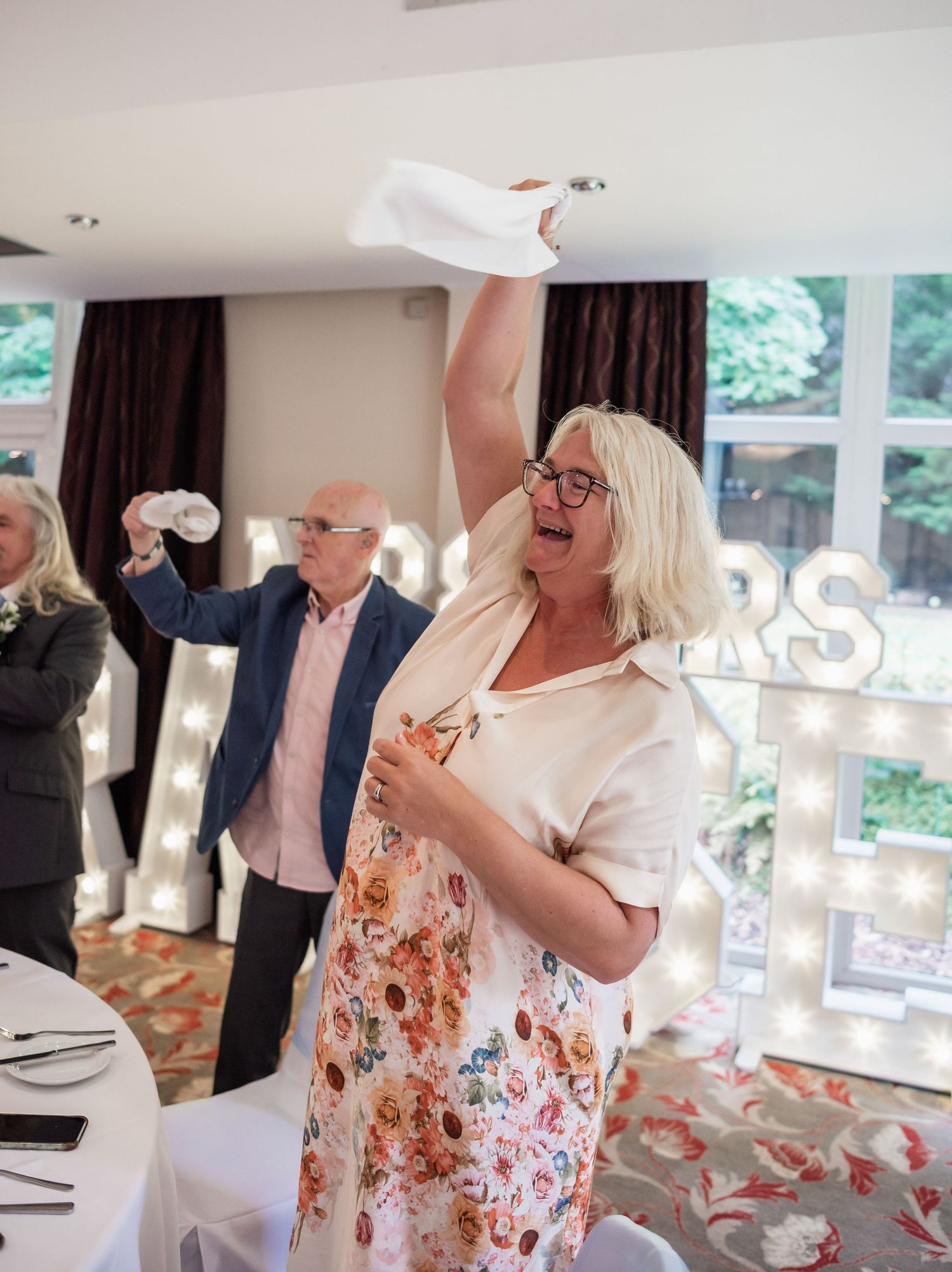 Wedding guest in floral dress joyfully celebrates during reception festivities.