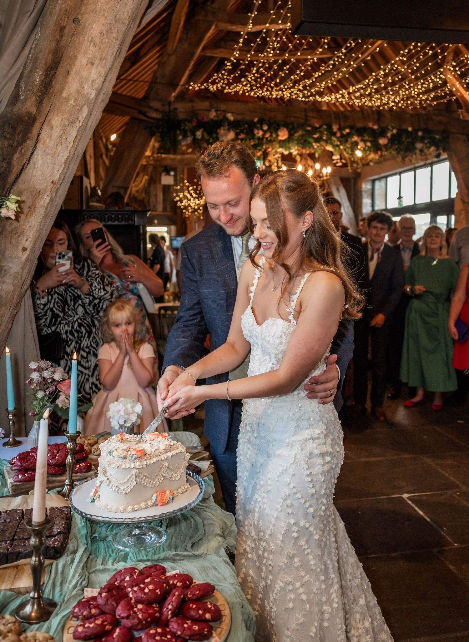 Couple cutting their wedding cake under warm string lights in a rustic venue.
