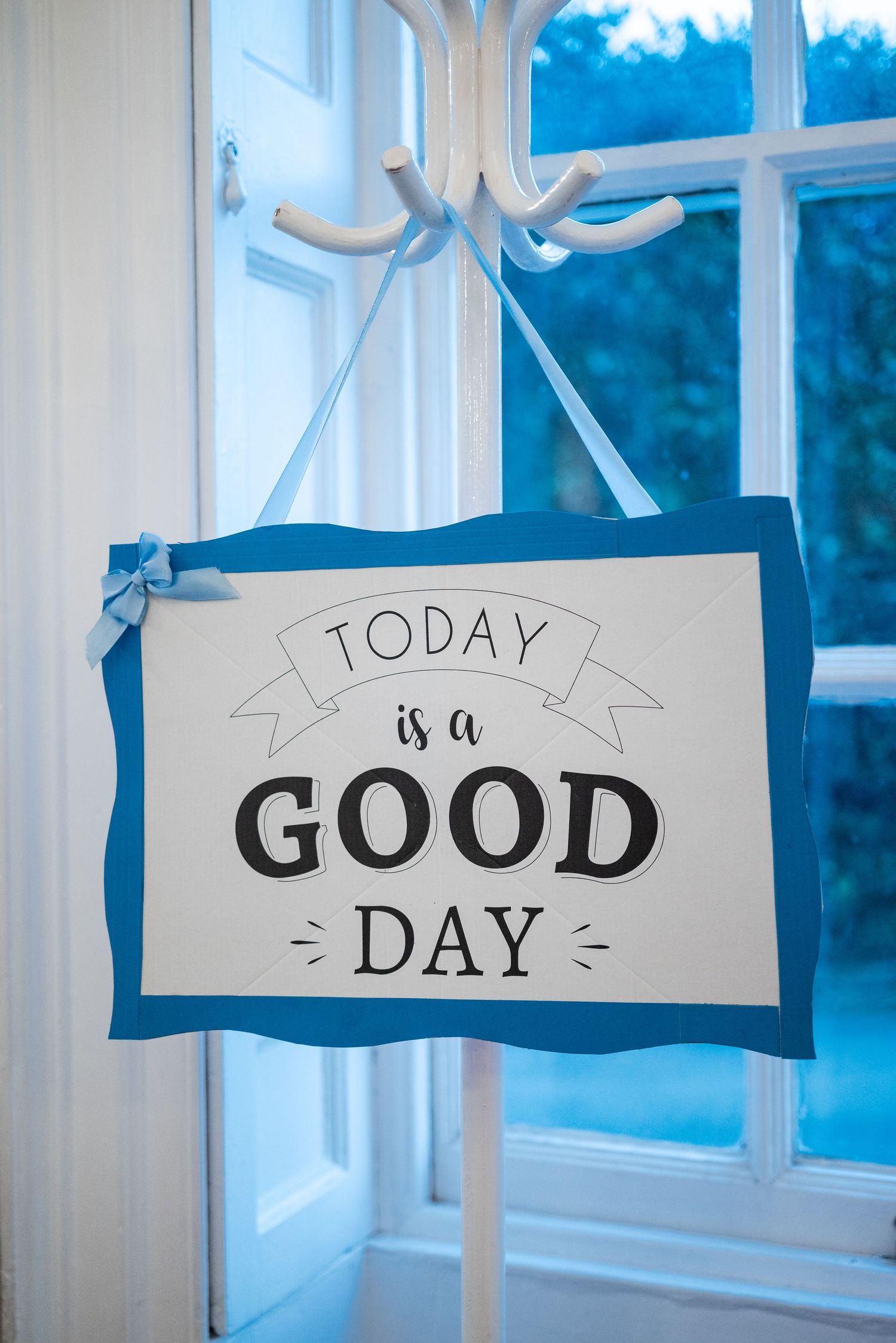 Handmade banner signs spelling 'Today is a Good Day' hanging in front of bright windows.